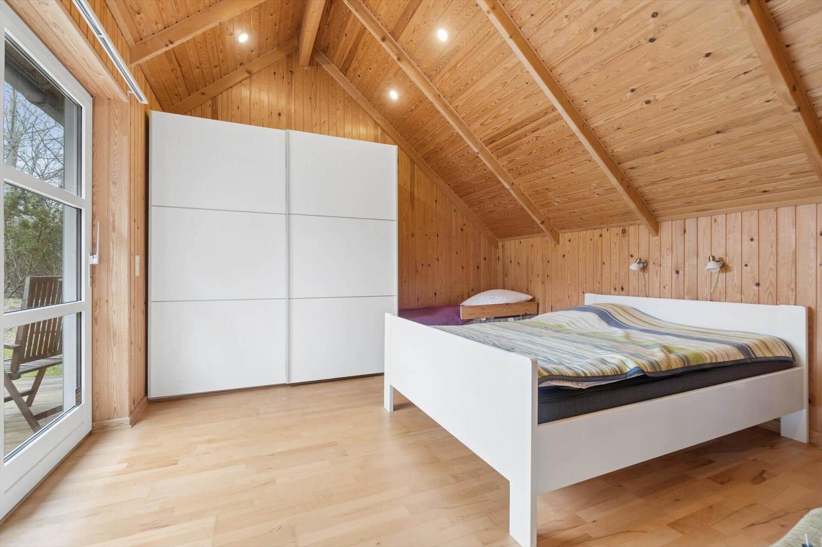 Schlafzimmer mit weißem Bett, Schwebetüren und Holzwandverkleidung unter schrägem Dach