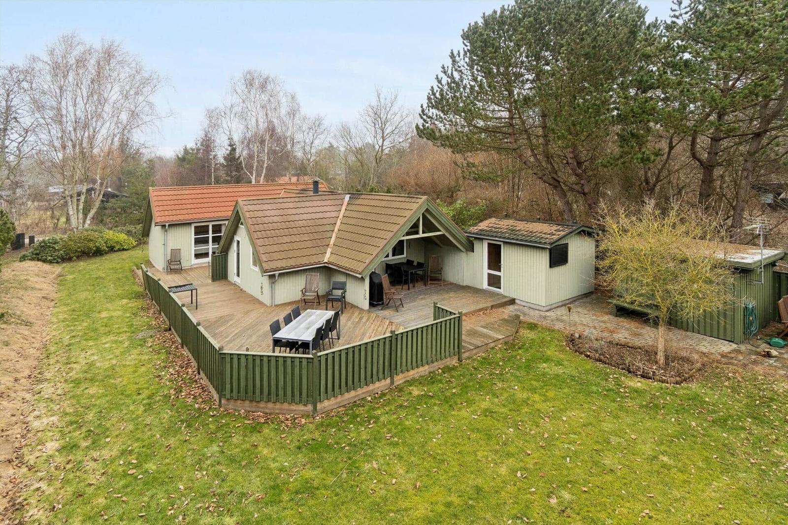 Haus mit Terrasse, Grill und Garten. Umgeben von Bäumen und Grasfläche.