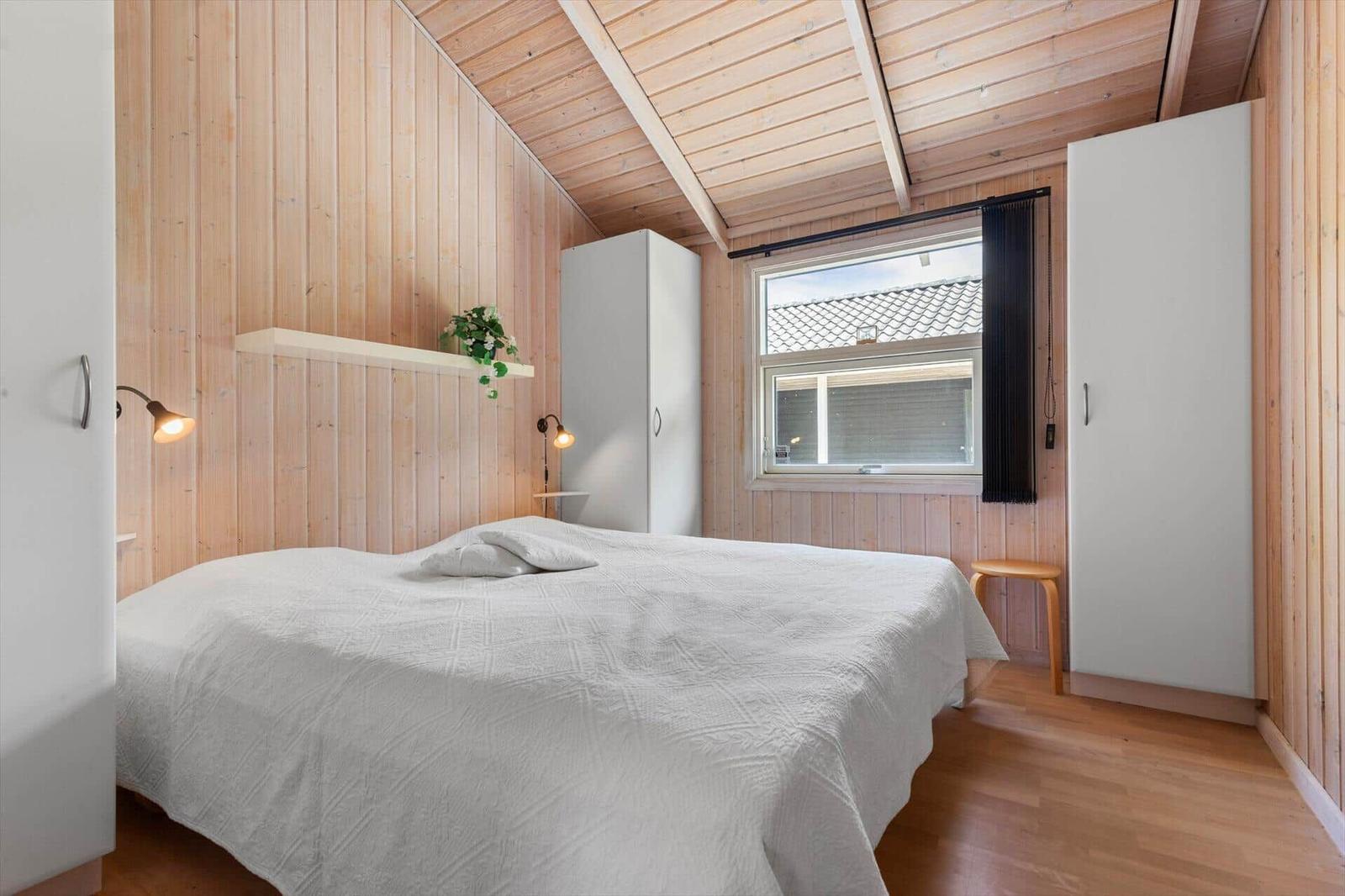 Schlafzimmer mit Holzwand, Bett, Fenster und Schränken.