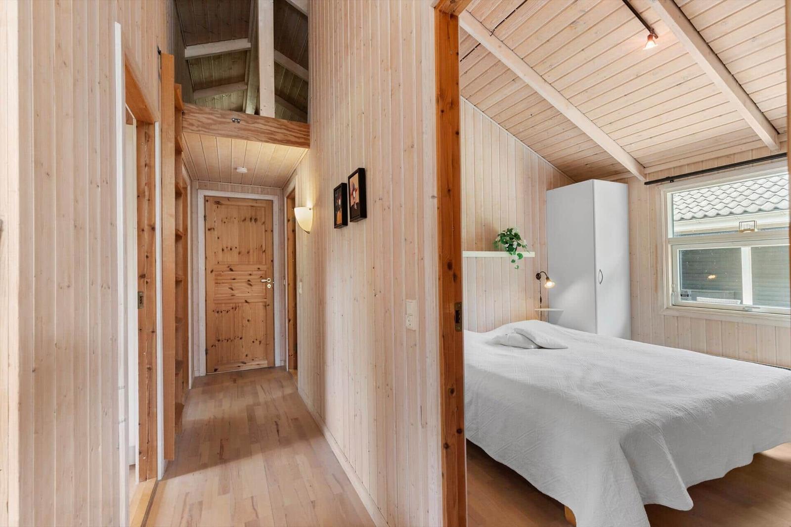 Schlafzimmer mit weißem Bett und Holzwand. Flur mit Tür und Wandbildern.