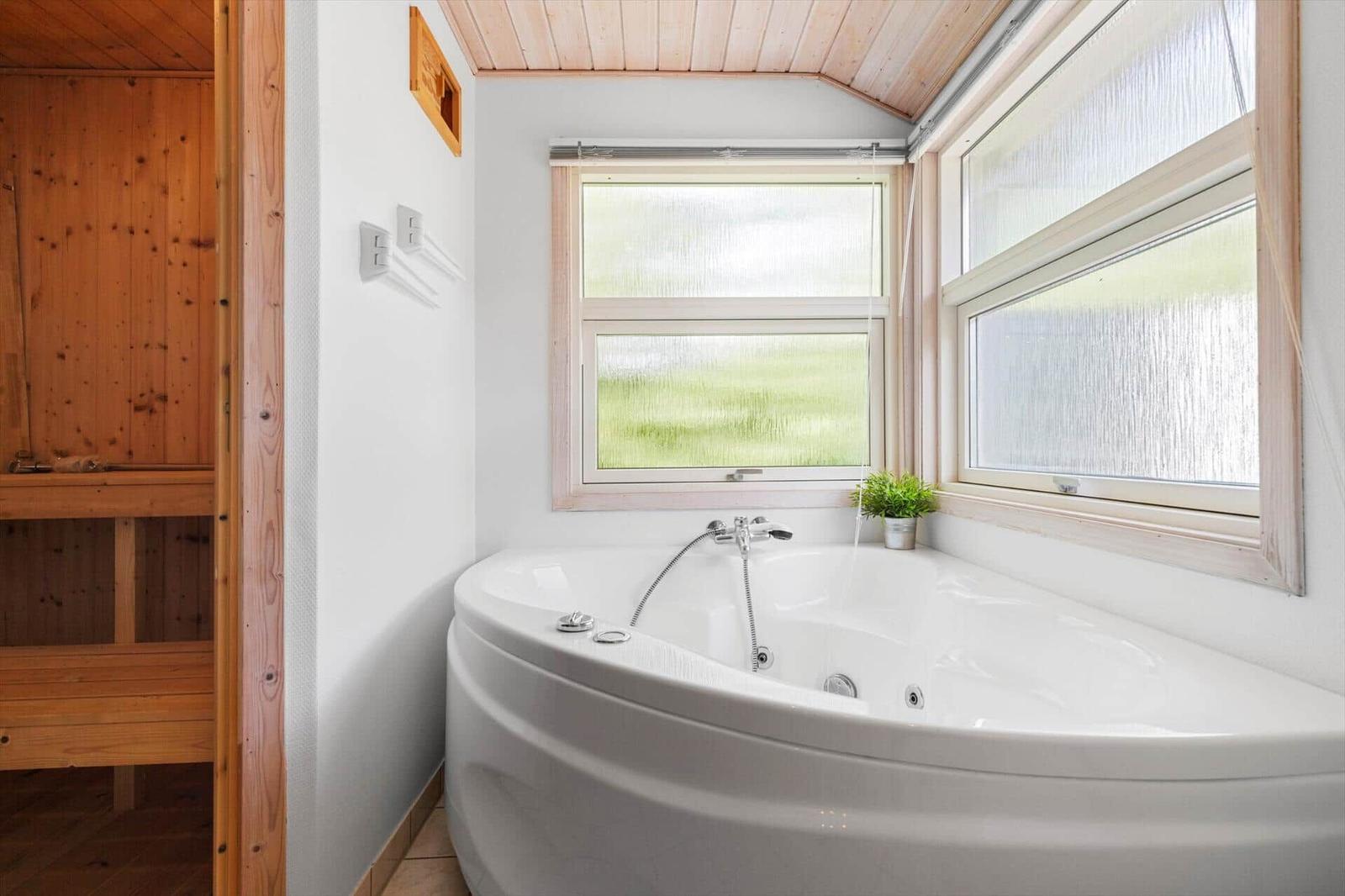 Eckbadewanne mit Duschbrause, zwei Fenstern und Holzverkleidung an der Wand.