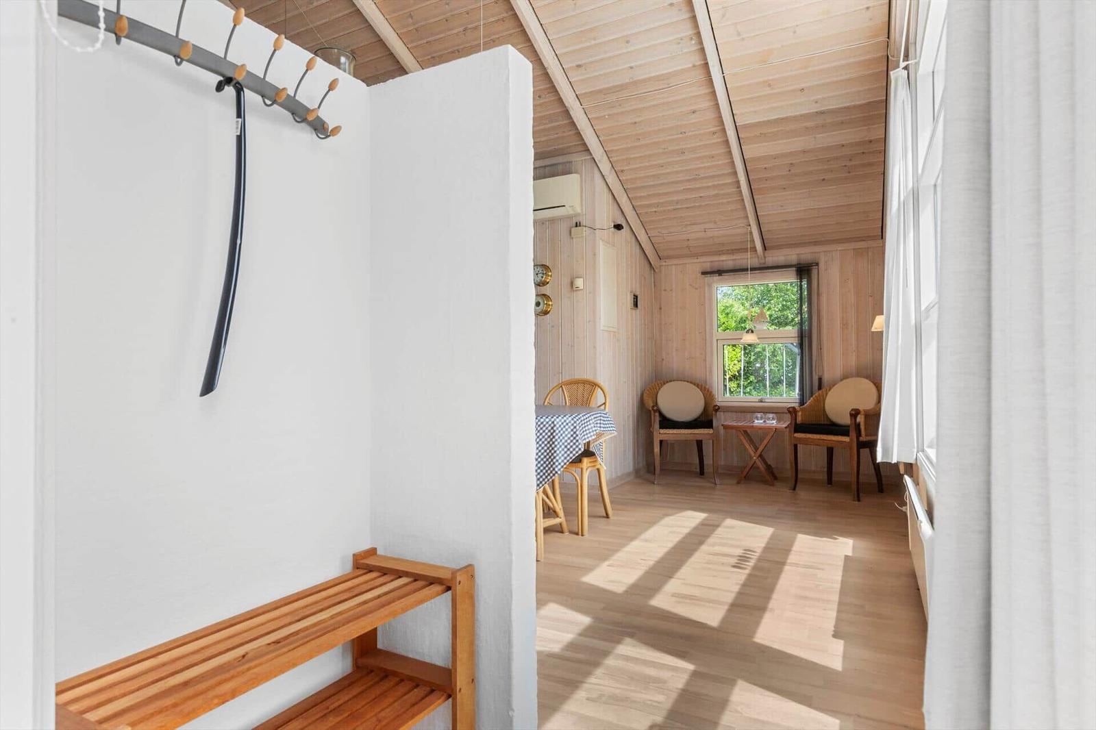 Raum mit Holzdecke, Tisch, Stühle und Fenster. Ankleidebereich mit Bänke und Haken.