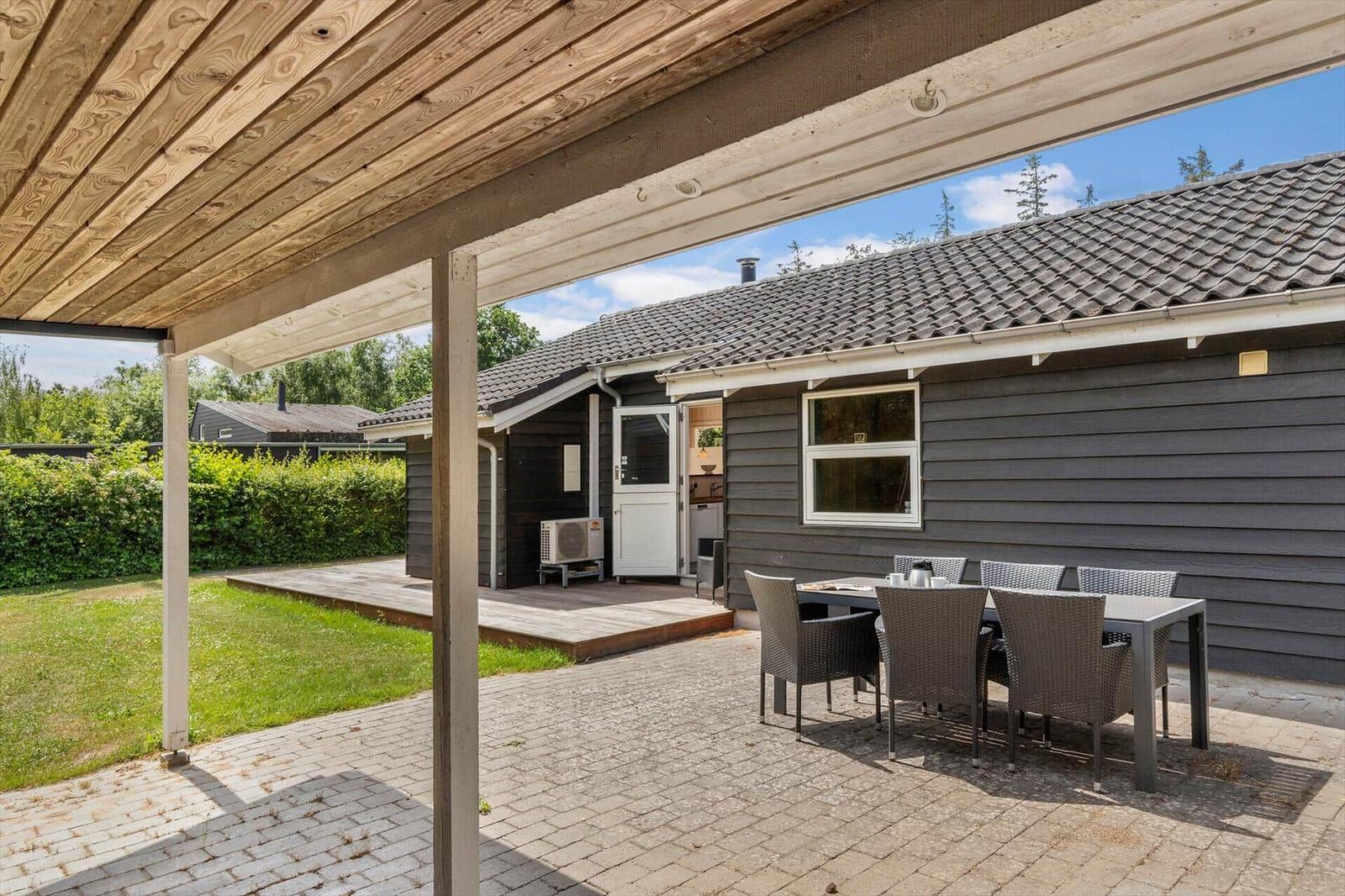 Terrasse mit Tisch und Stühlen vor einem Haus mit Holzveranda und Garten.