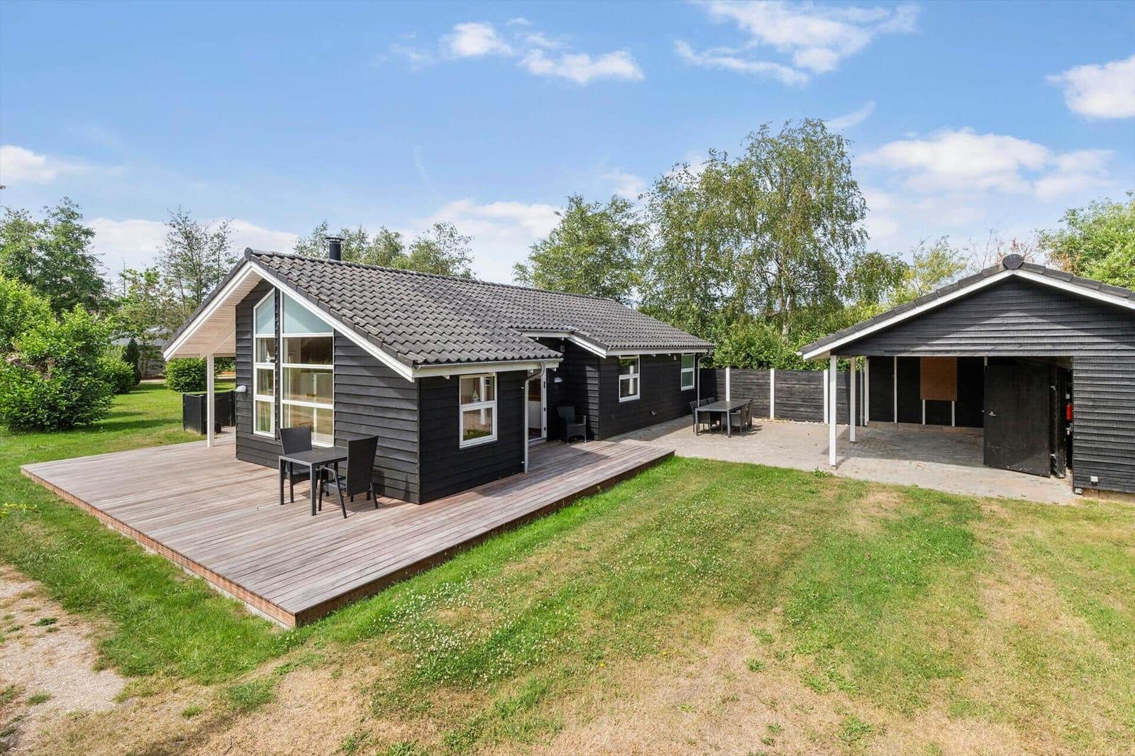 Moderne schwarze Holzhütte mit großem Balkon und Grillplatz im Garten.