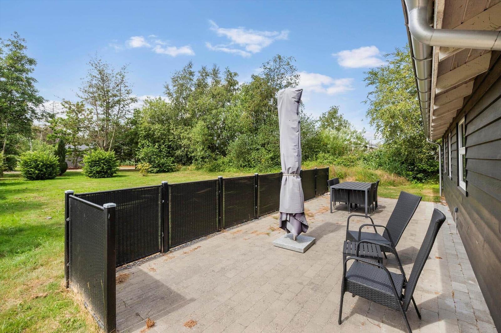 Terrasse mit Garten, Tisch, Stühlen und geschlossenem Sonnenschirm.