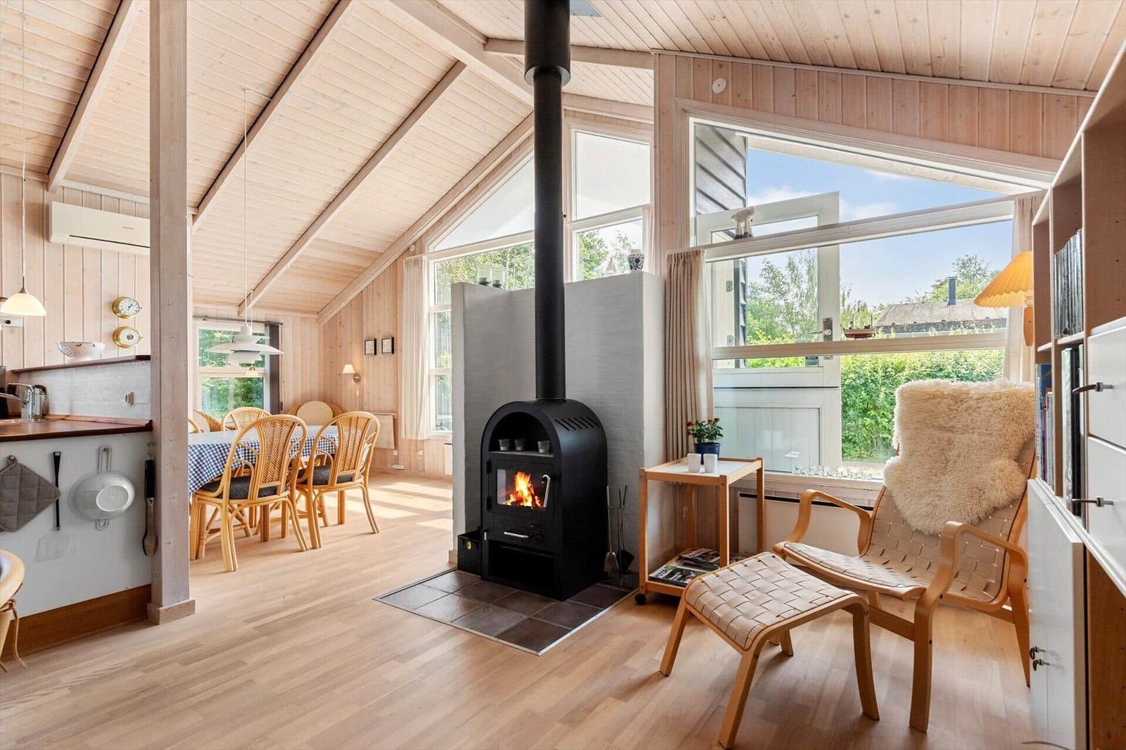 Wohnbereich mit Kamin, Sitzgelegenheit und Blick auf Garten. Küche und Essbereich sind sichtbar.