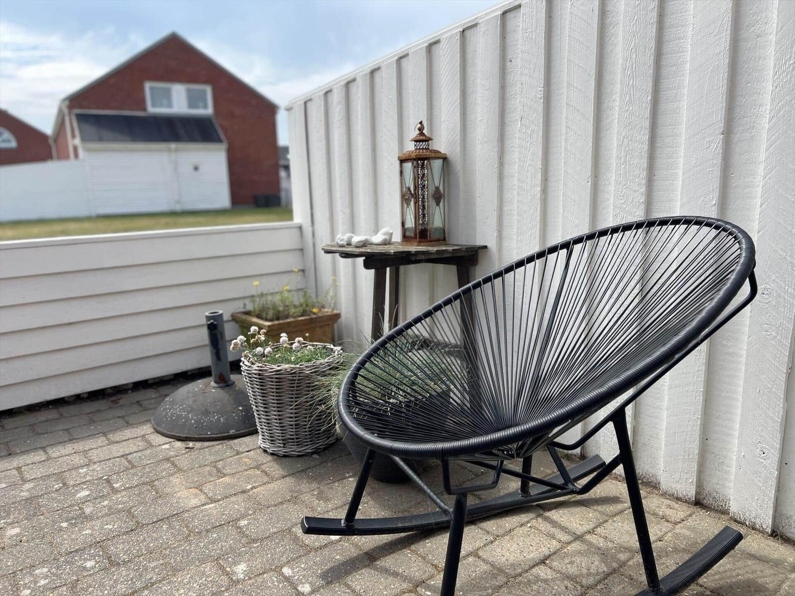 Schwarze Schaukelstuhl auf Terrasse mit Pflanzen und Laterne an weißer Wand.