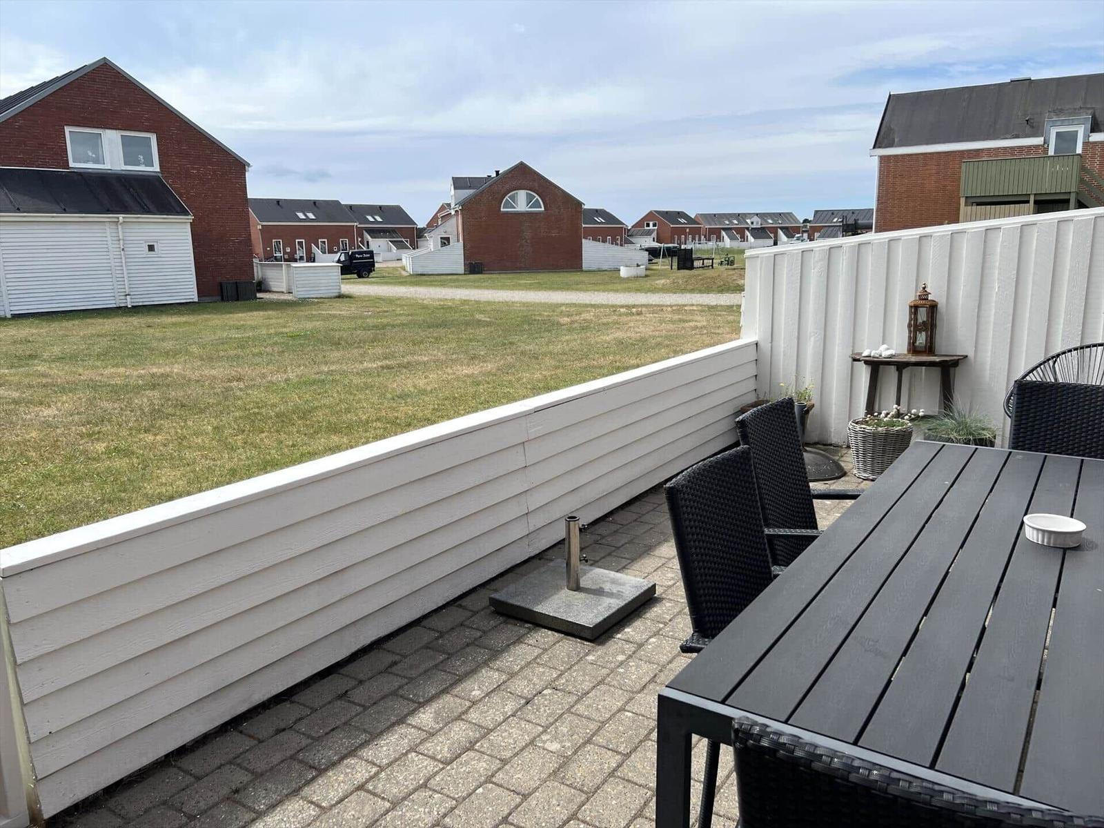 Terrasse mit Tisch und Stühlen, weißer Zaun, Blick auf Gras und Häuser