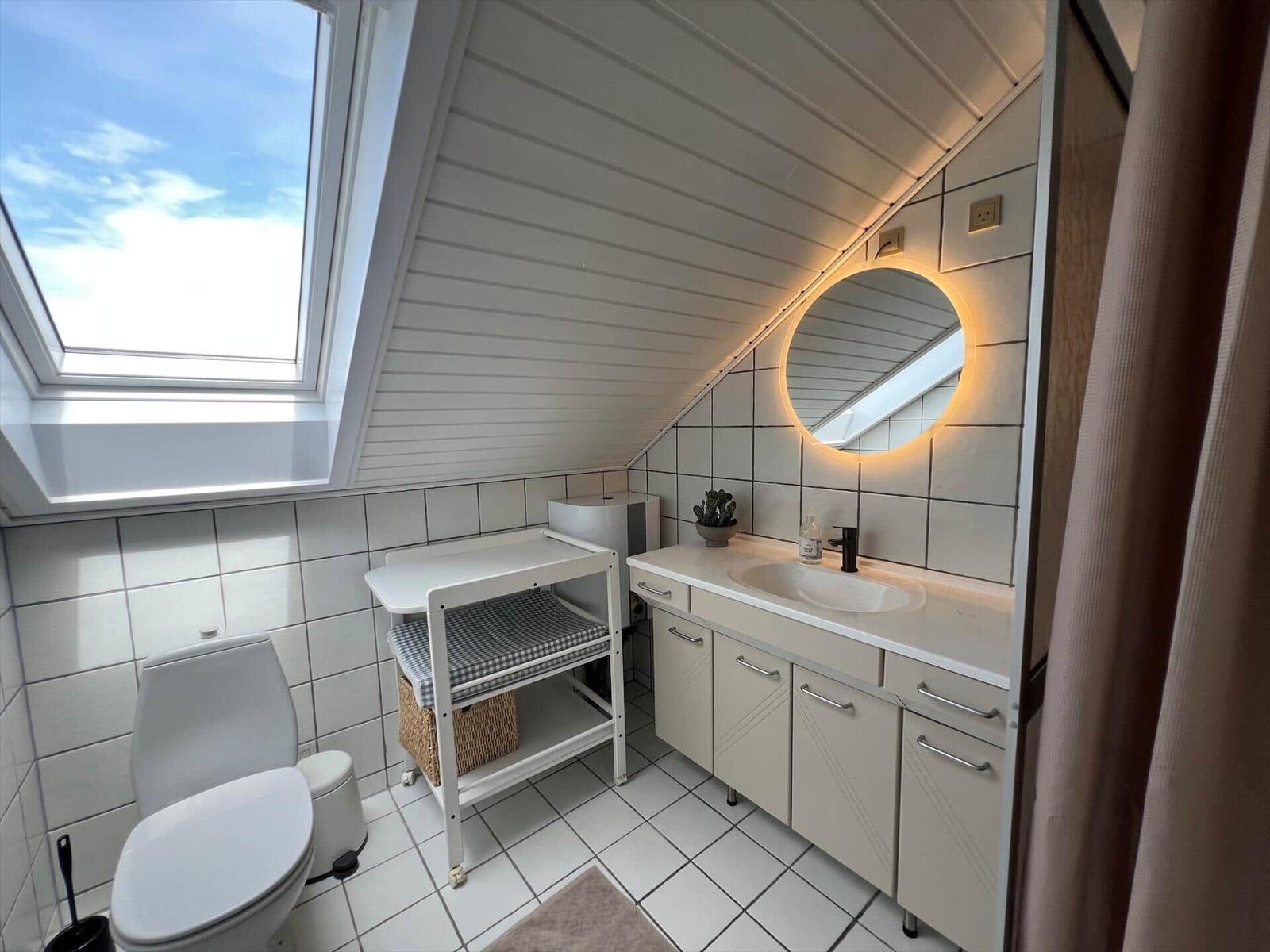 Badezimmer mit Dachfenster, Waschbecken, Spiegel und Toilette.