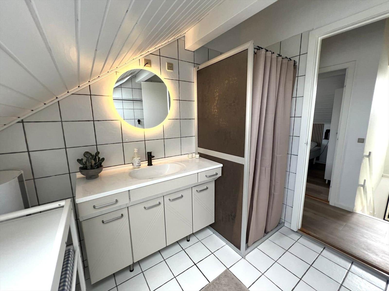 Badezimmer mit Waschtisch, Spiegel und Dusche mit Vorhang.