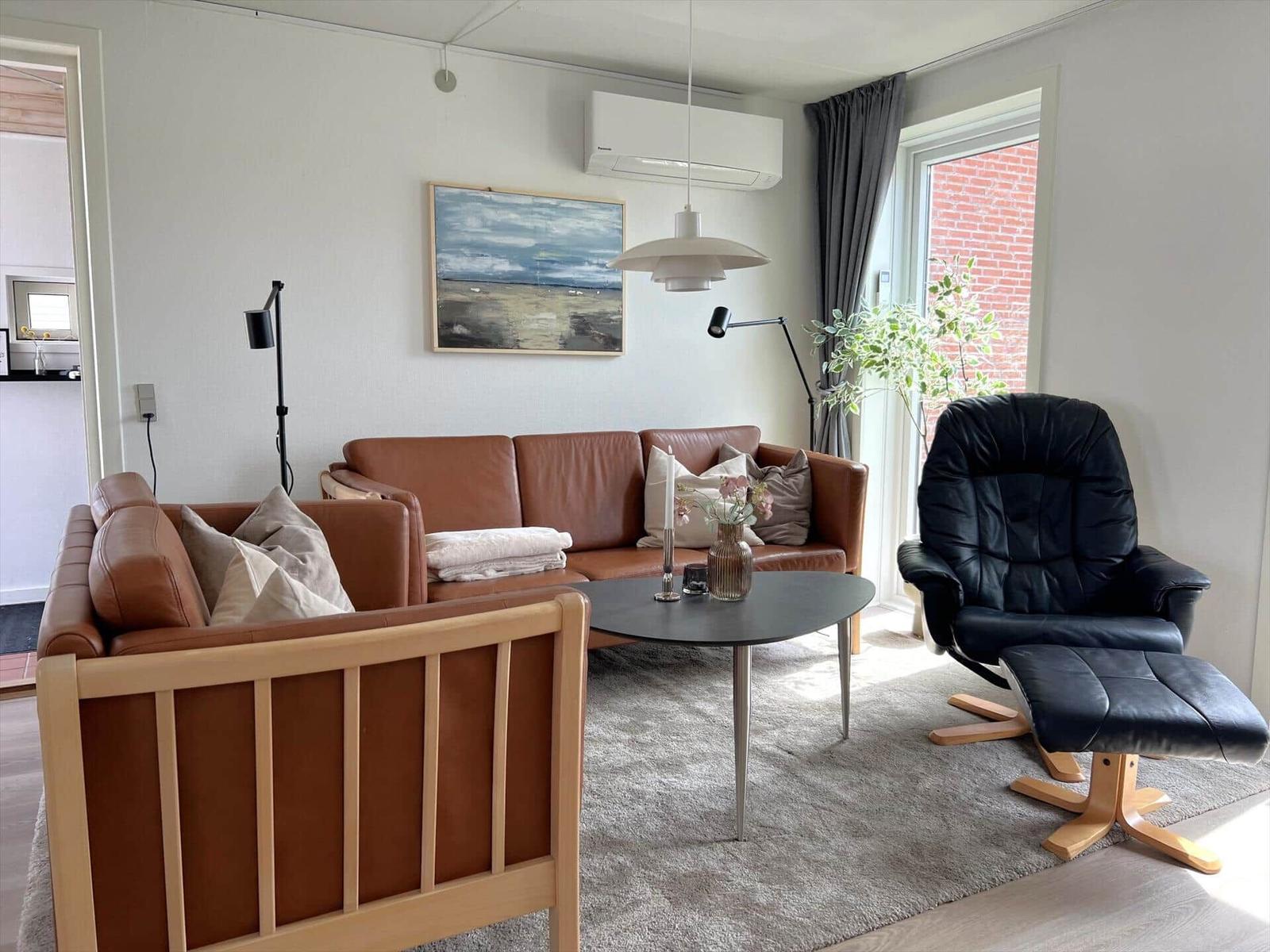 Wohnzimmer mit braunem Sofa, schwarzer Sessel und Tisch. Wandbild und Fenster sichtbar.