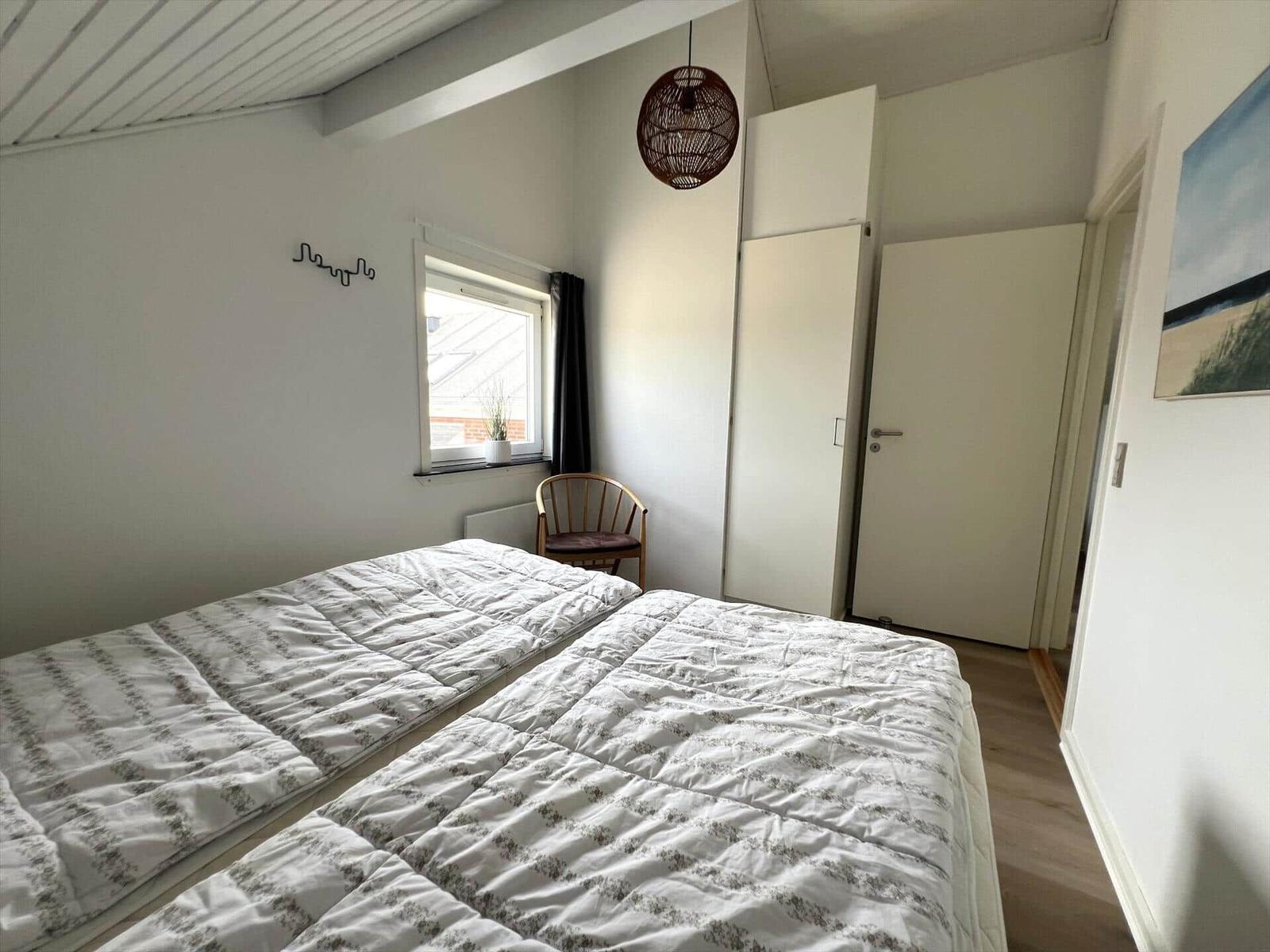 Schlafzimmer mit Doppelbett, Fenster, Stuhl und Kleiderschrank.