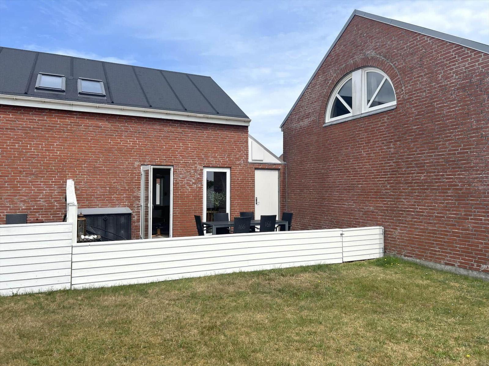 Rotes Backsteinhaus mit Terrasse und Garten. Weiße Umzäunung und Sitzgruppe.