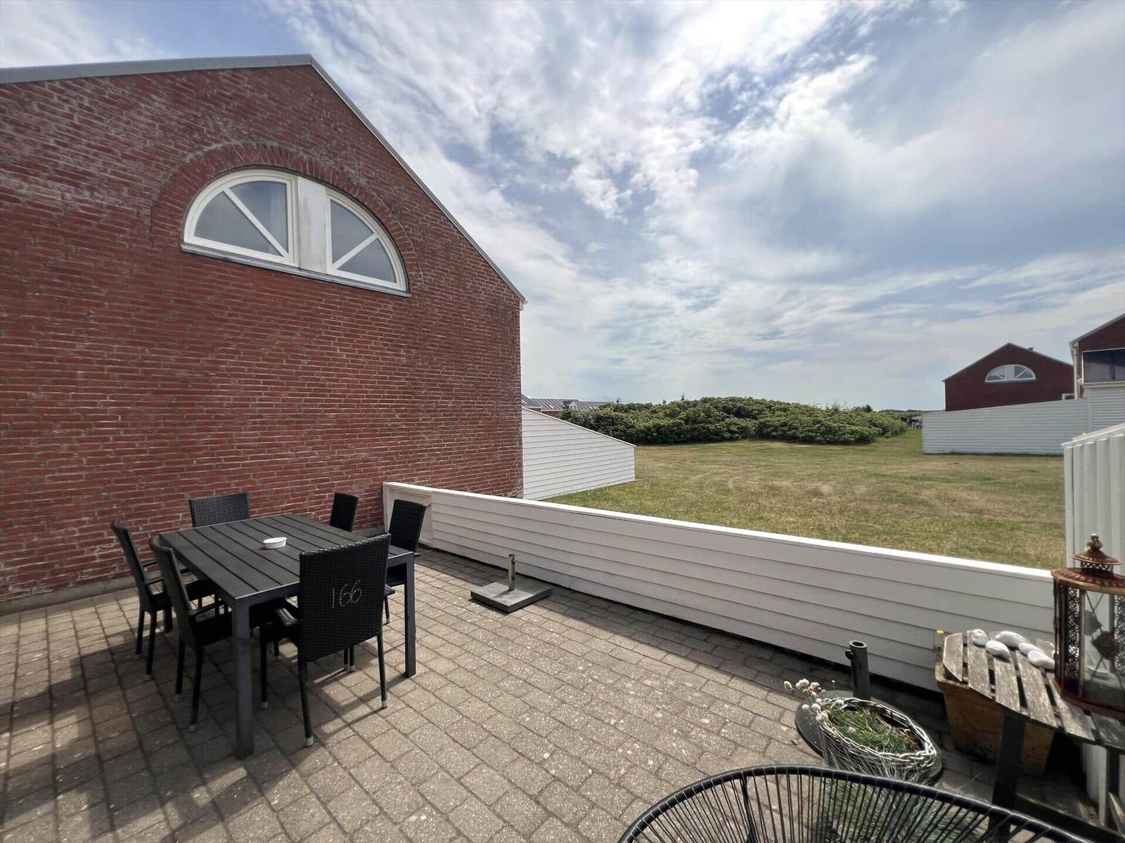 Terrasse mit Tisch und Stühlen neben rotem Backsteinhaus mit Blick auf Grünfläche.