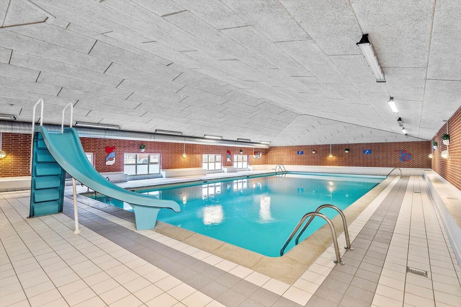Indirekter Pool mit Rutsche und Metallstufen in einem Innenbereich mit Ziegelwand.