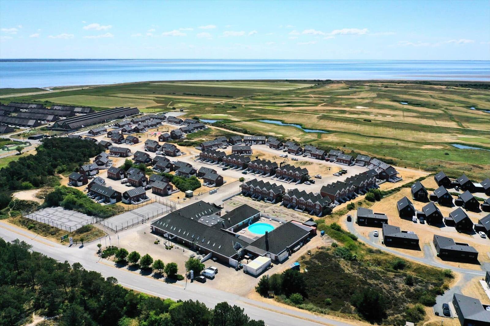 Aerial view of vacation homes near water with pool and green fields.