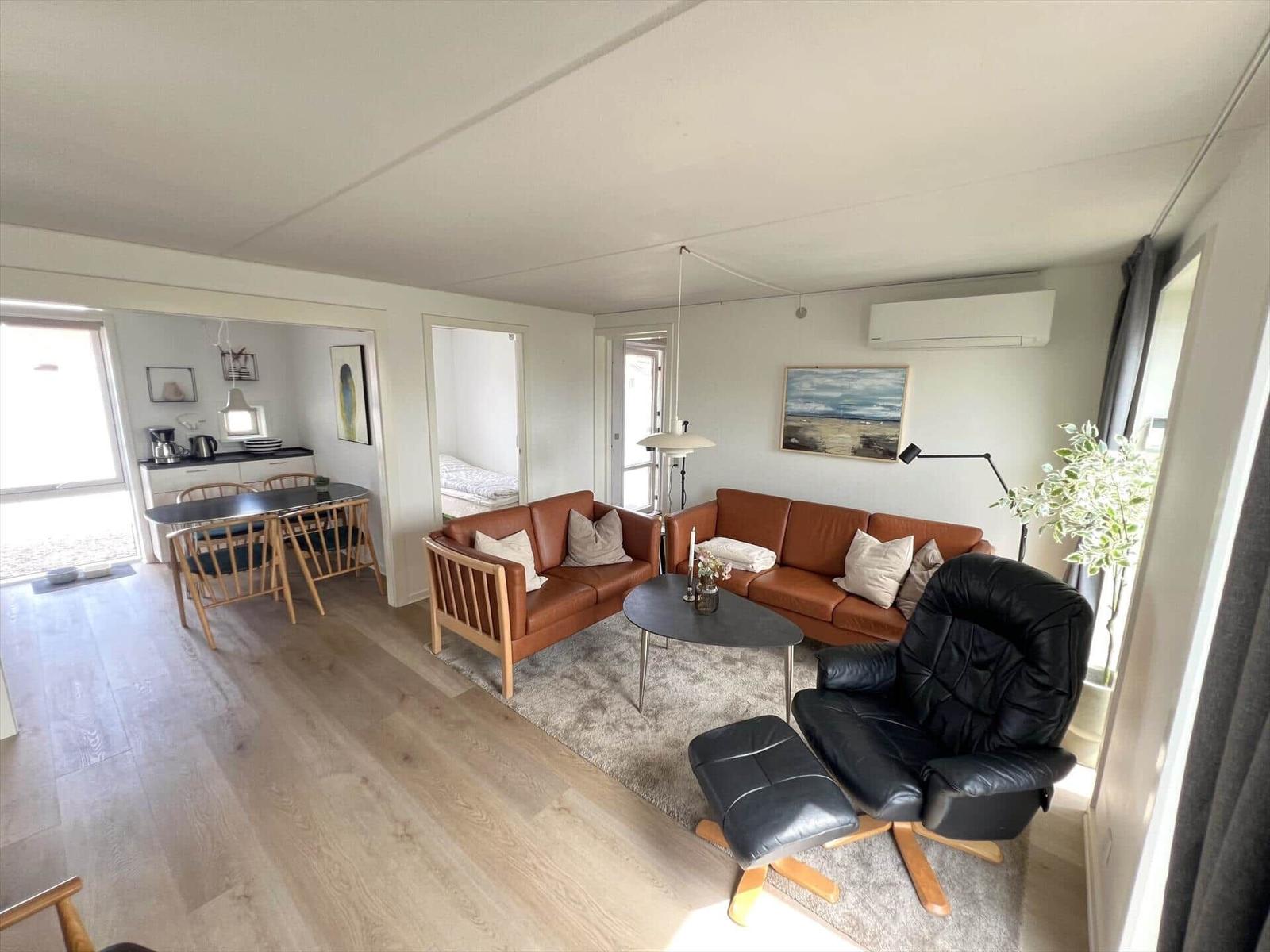 Wohn- und Essbereich mit braunen Sofas, schwarzer Ledersessel und Holzboden.