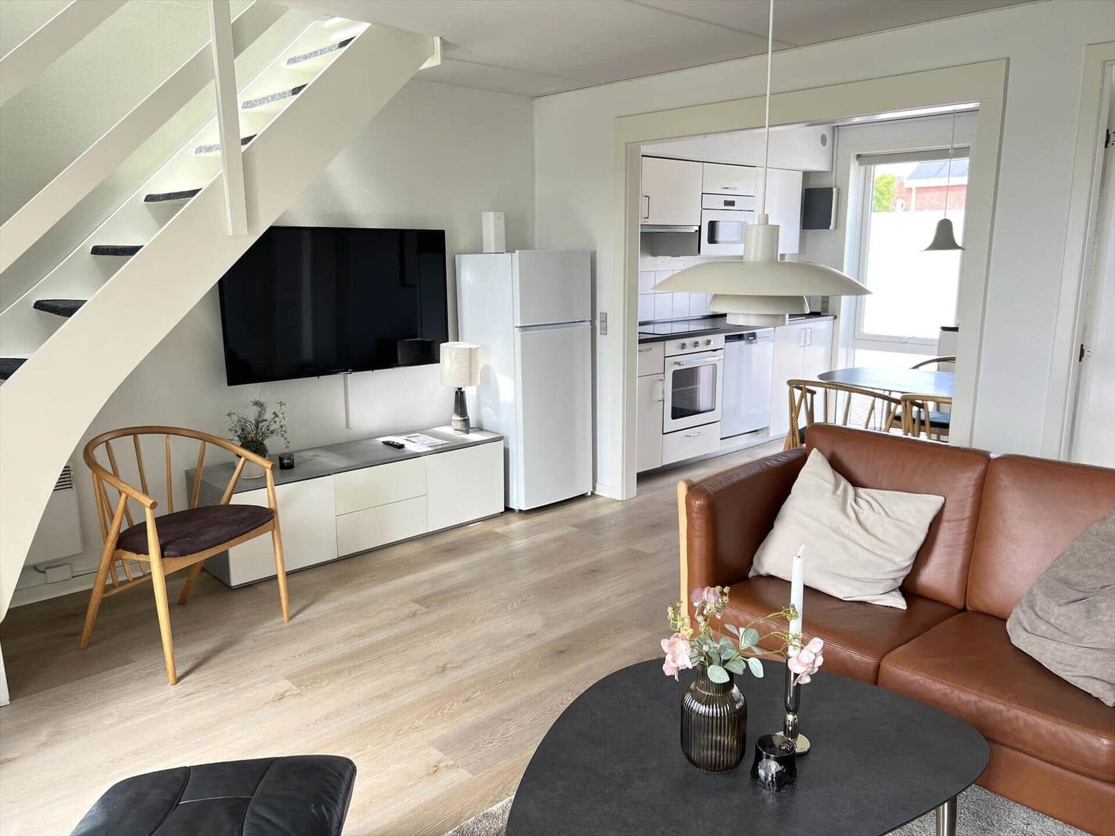 Wohnzimmer mit braunem Sofa, Fernseher und Küchenbereich im Hintergrund.