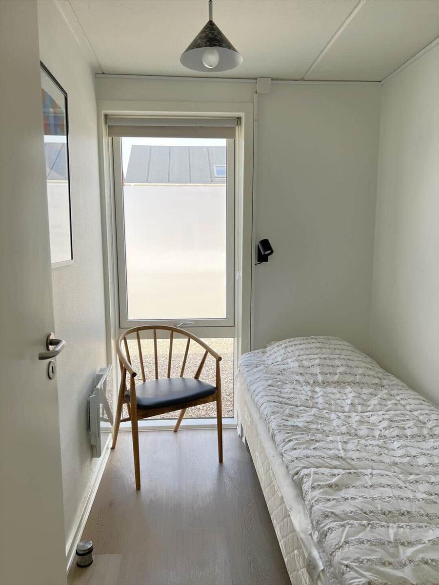 Schlafzimmer mit Bett, Stuhl und Fenster. Holzfußboden und Deckenleuchte.