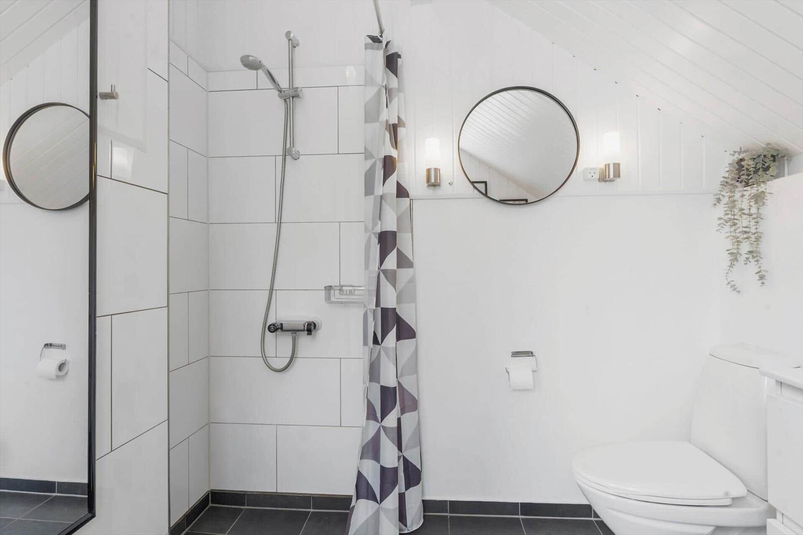 Badezimmer mit Dusche, Toilette und runden Spiegeln an der Wand.
