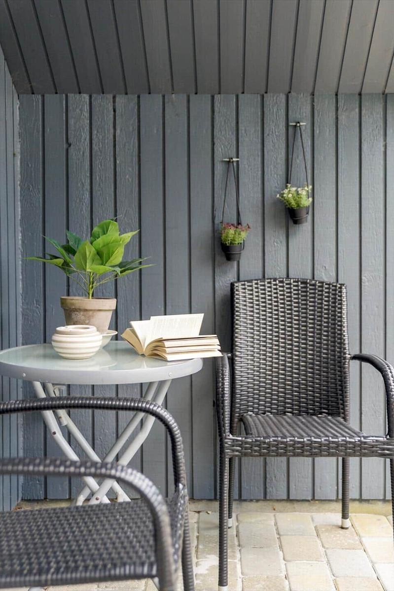 Terrasse mit Tisch, Stühlen und Pflanzen an grauer Holzwand.