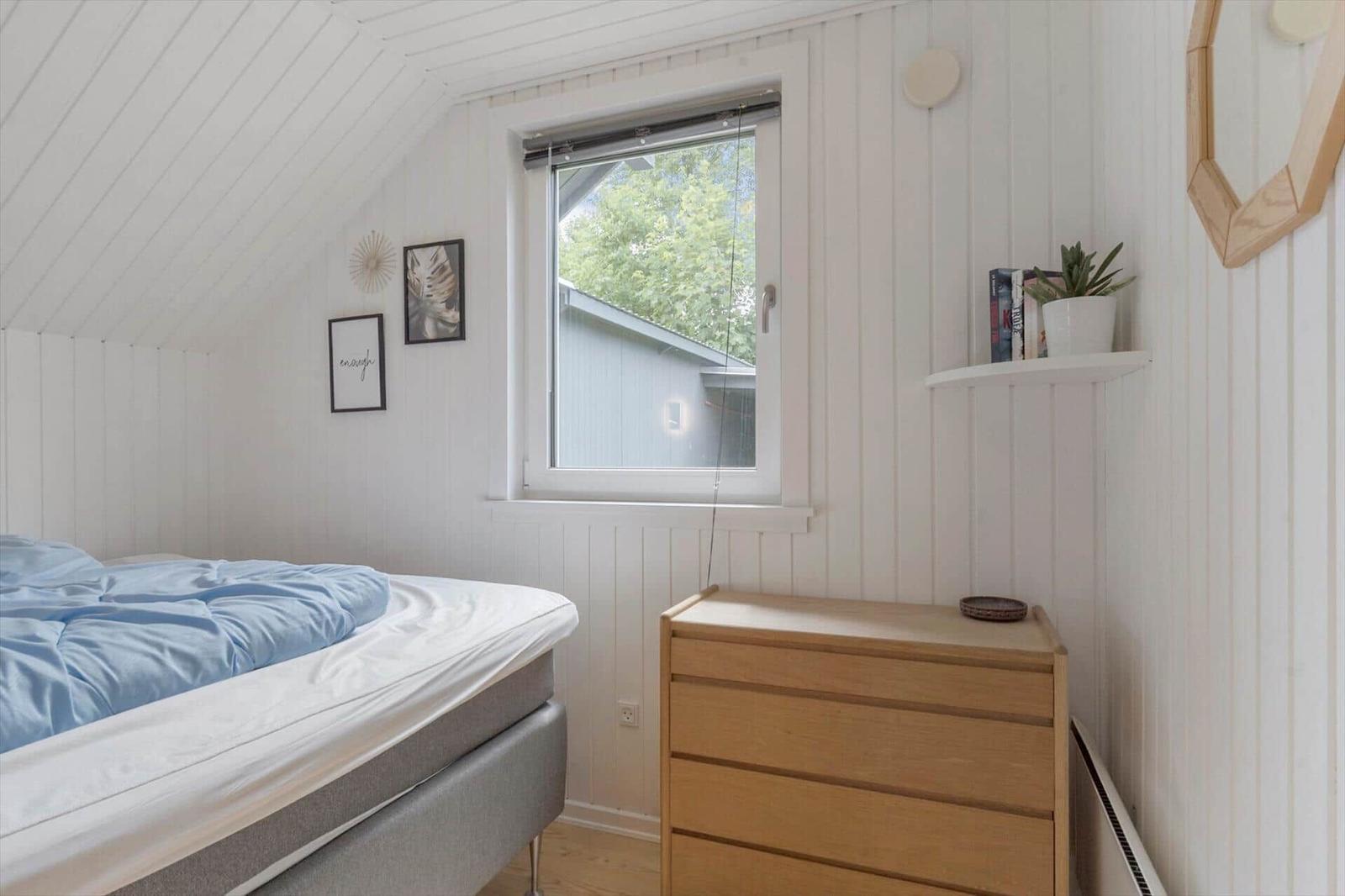 Schlafzimmer mit Bett, Schrank und Fenster. Wandgestaltung mit Bildern und Pflanze.