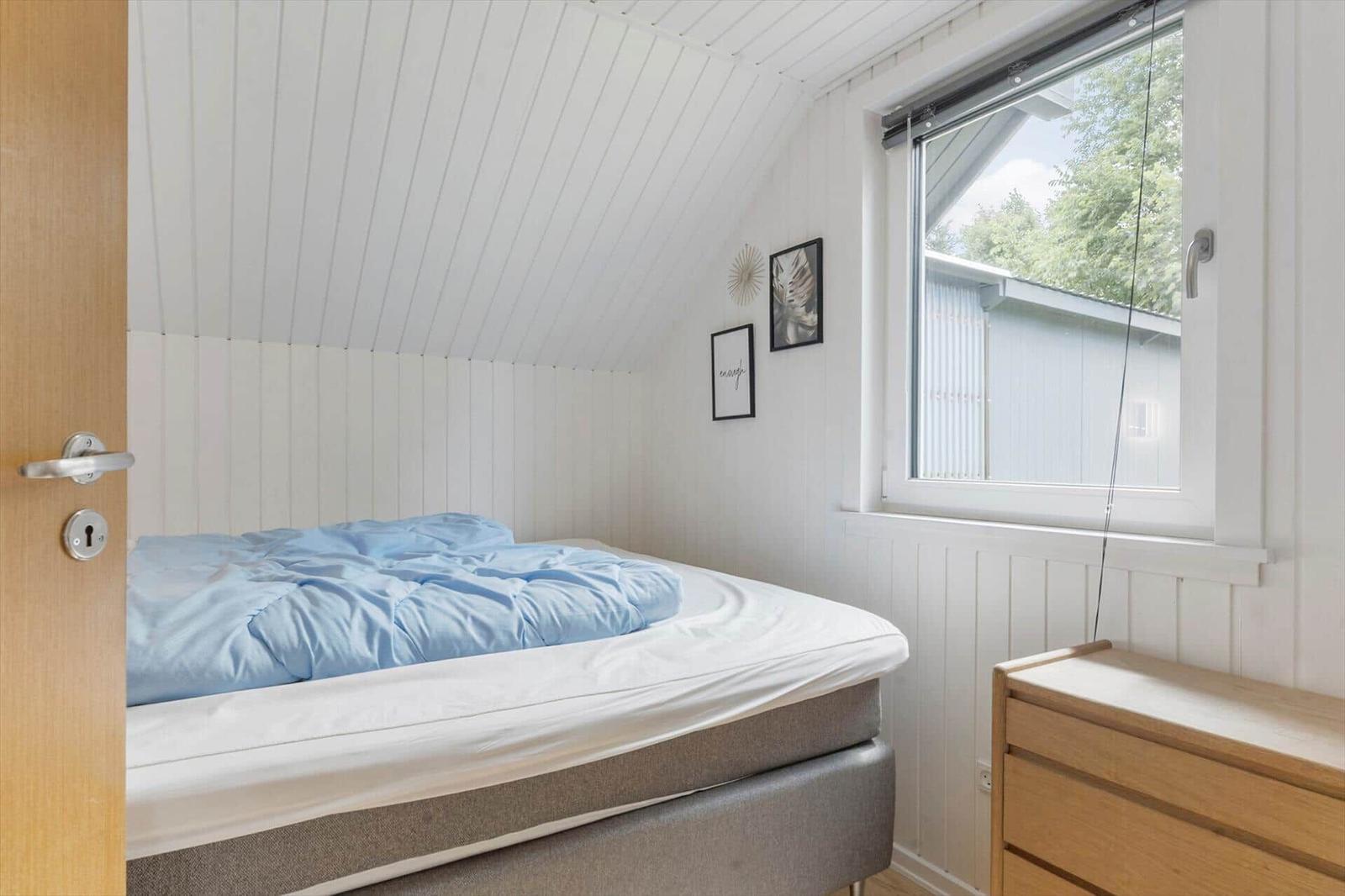 Schlafzimmer mit Bett, Fenster und Kleiderschrank. Weiße Wände und Holzdetails.
