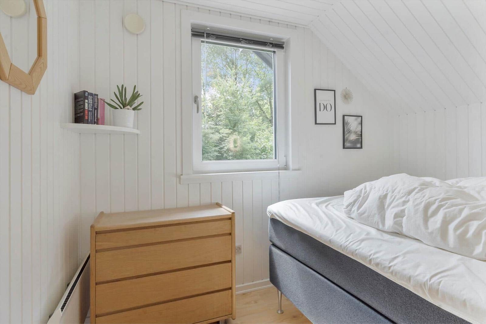 Schlafzimmer mit Dachbodenfenster, Bett und Holzschrank. Wand mit Bildern und Pflanze.