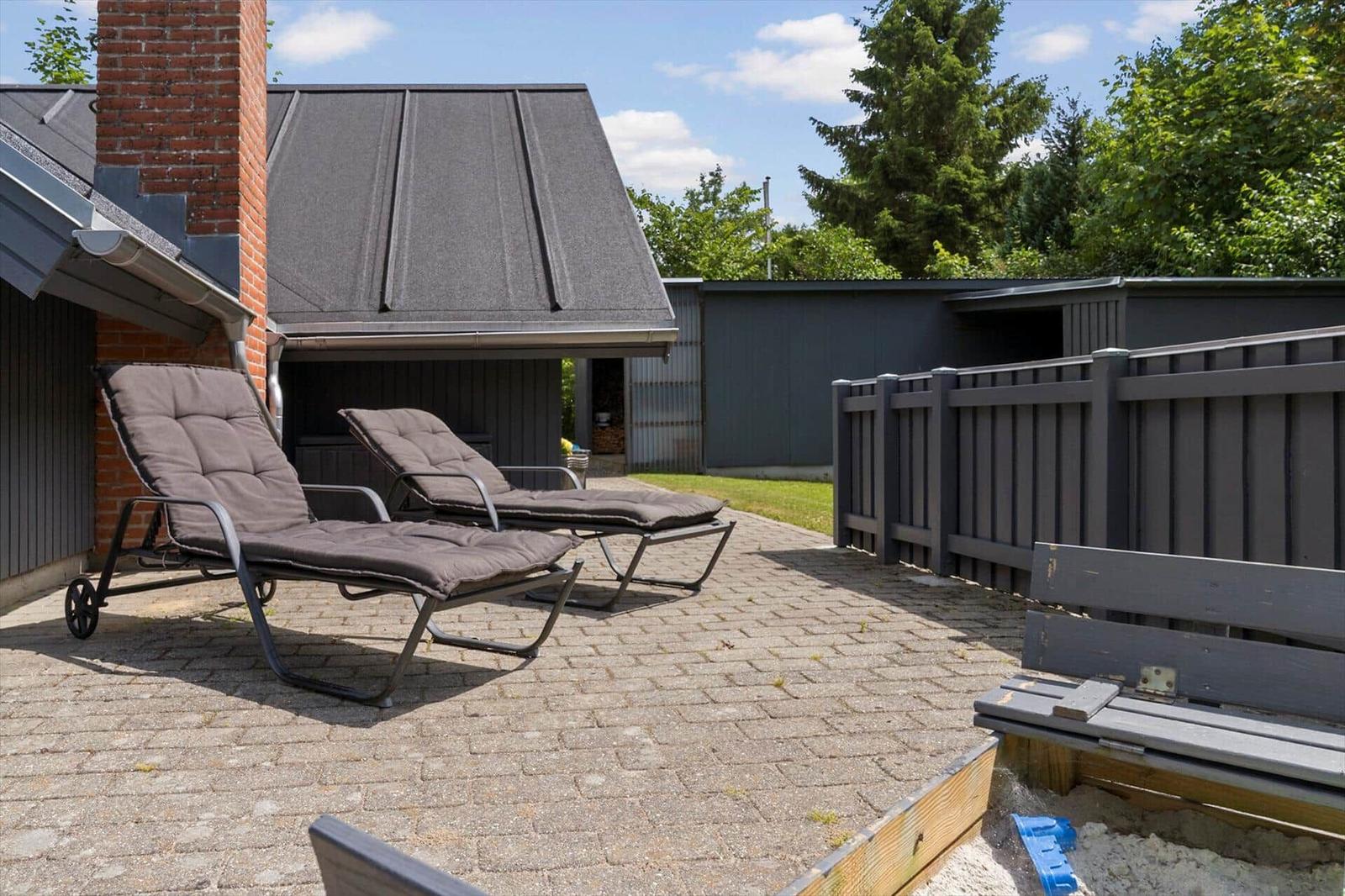 Terrasse mit zwei Liegestühlen, Holzbank und Sandkasten. Hinterhof mit Zaun und Grünfläche.