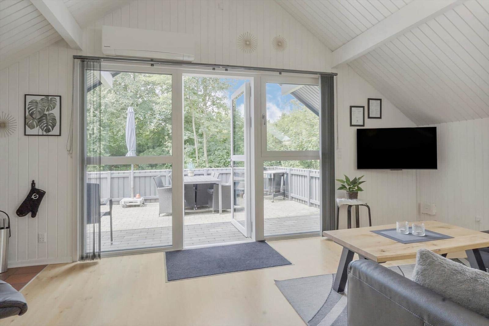 Wohnraum mit Glasfront zum Balkon, TV und Esstisch.