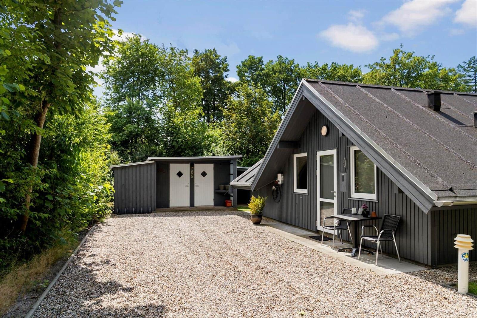 Holzhaus mit Terrasse, Grill und Grillplatz. Umgeben von Bäumen und Gras.