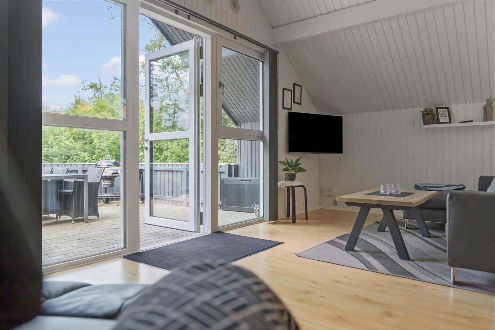 Wohnbereich mit Holzboden, TV und Blick auf Balkon mit Grill.