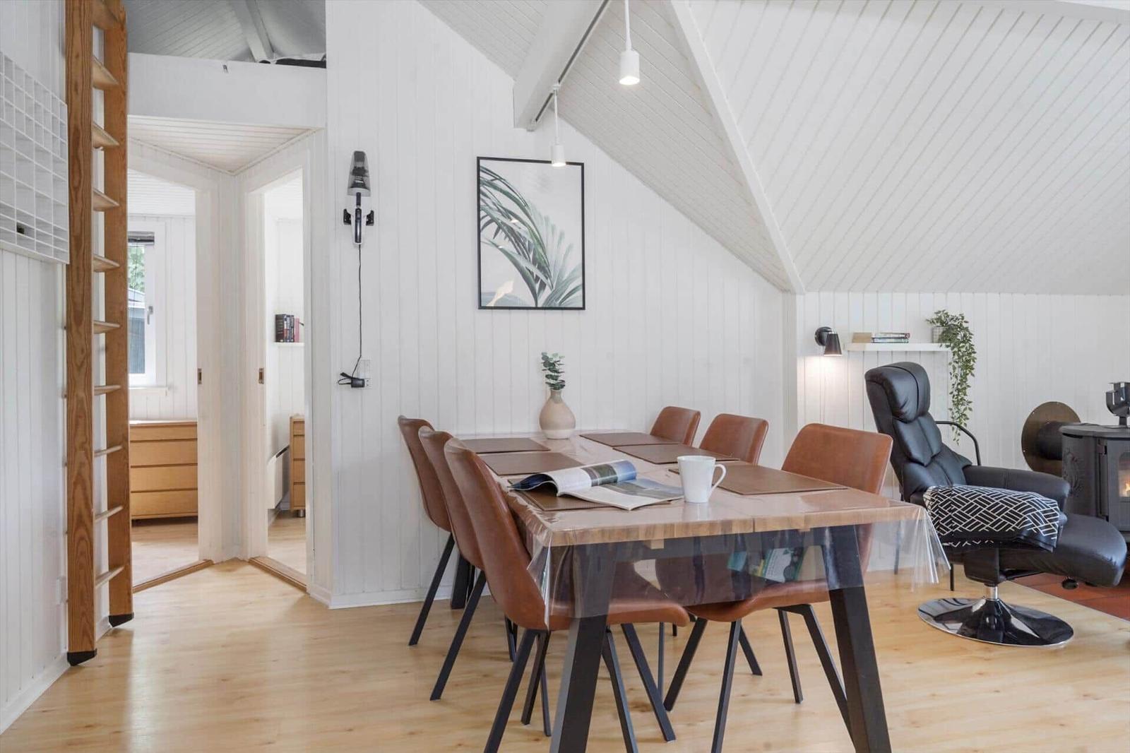 Essbereich mit Tisch, Stühlen und Sessel. Helle Wände, Holzboden und Dachschrägen.