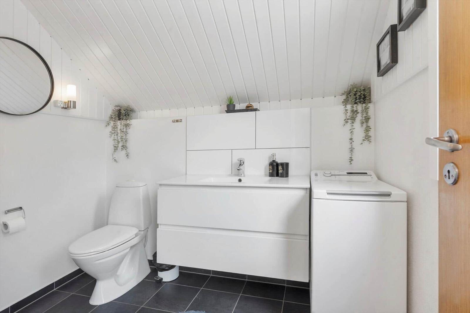 Badezimmer mit Toilette, Waschbecken und Waschmaschine. Weiße Wand- und Deckenverkleidung.
