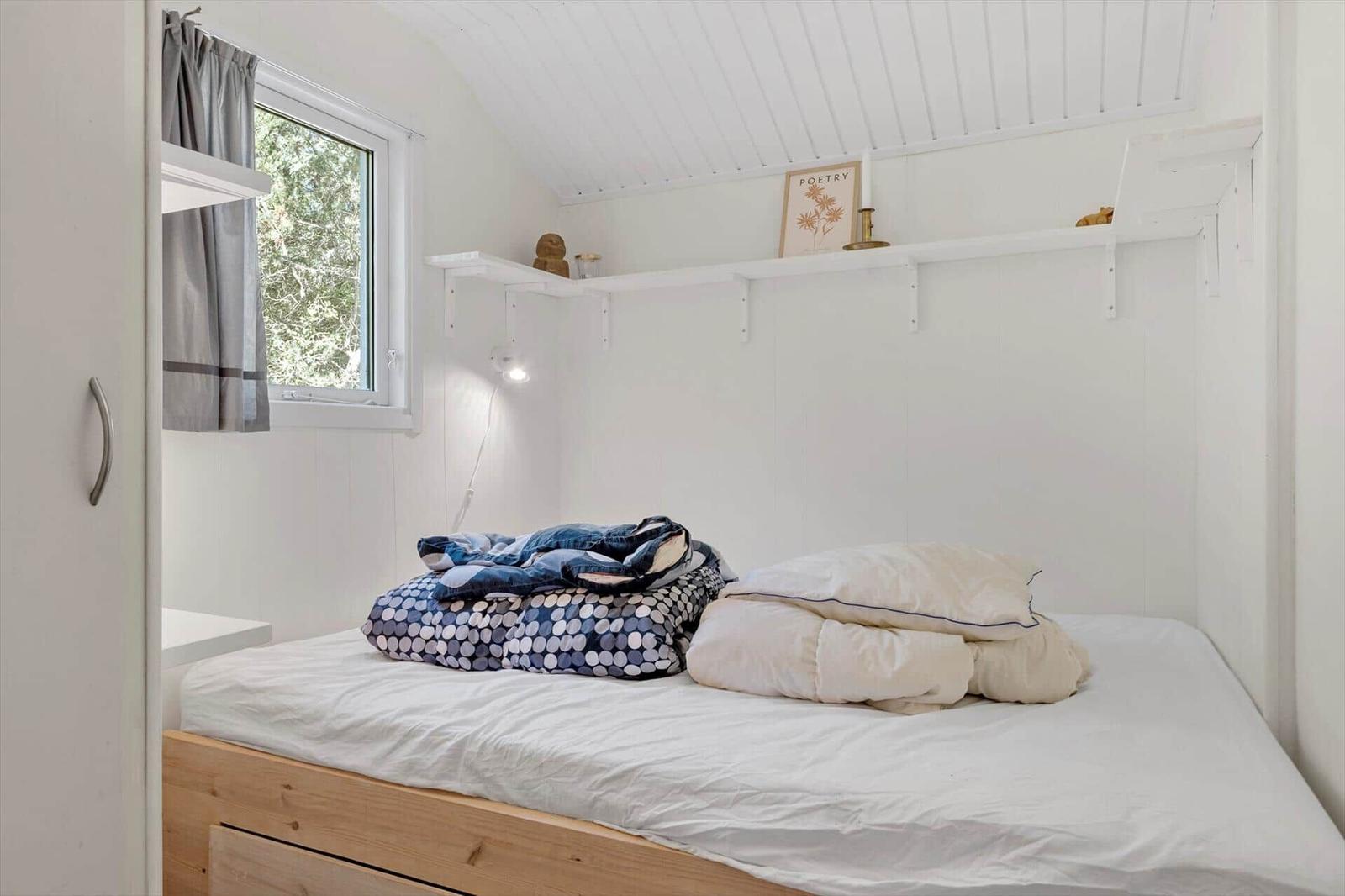 Schlafzimmer mit Bett, Fenster und Regal an der Wand.