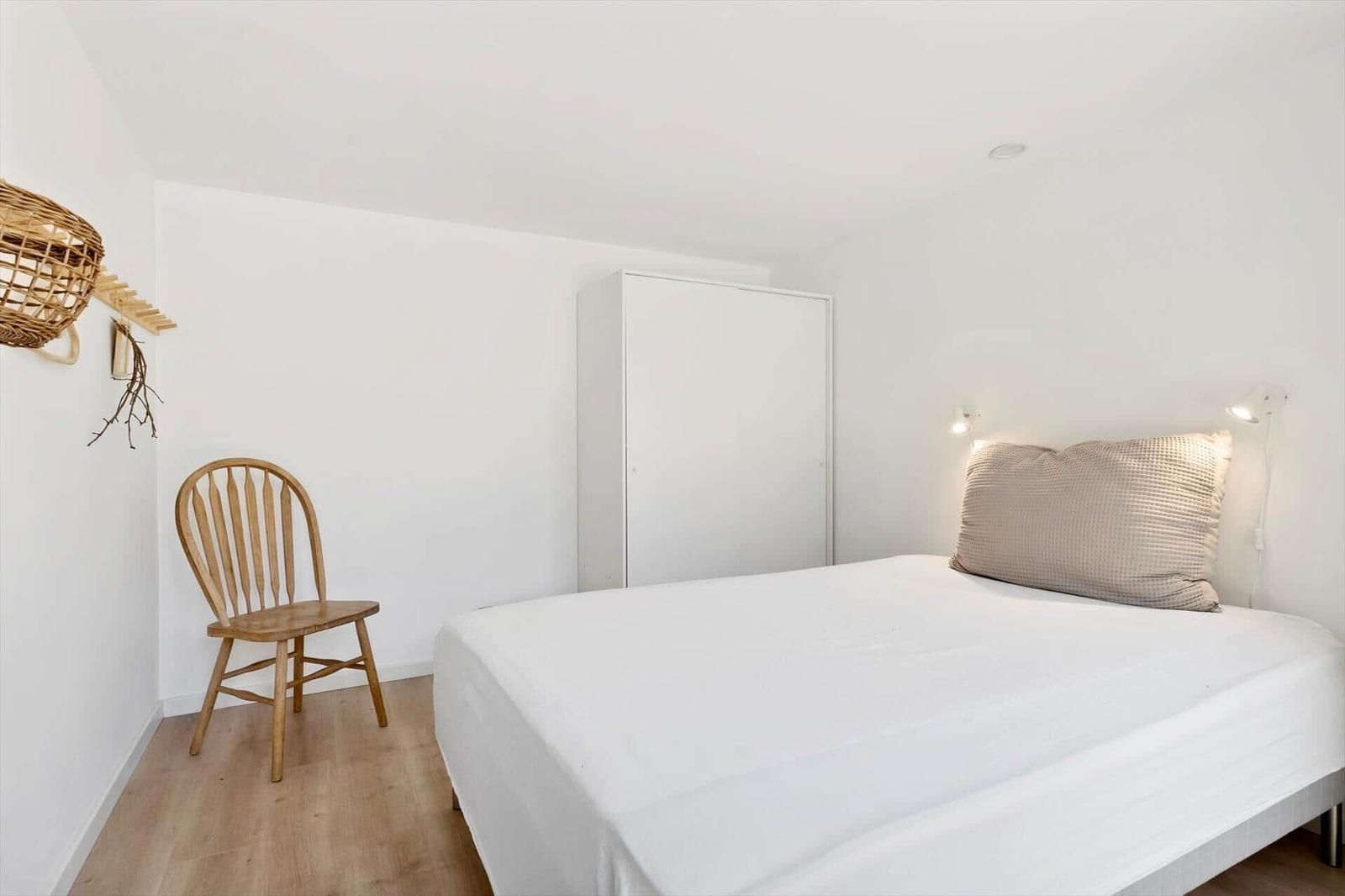 Ein Schlafzimmer mit Bett, Kleiderschrank und Stuhl. Wandlampe und Korb an der Wand.