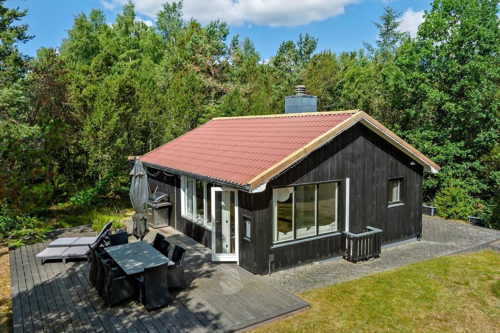 Holzhütte mit Terrasse, Grill und Blick in den Wald.