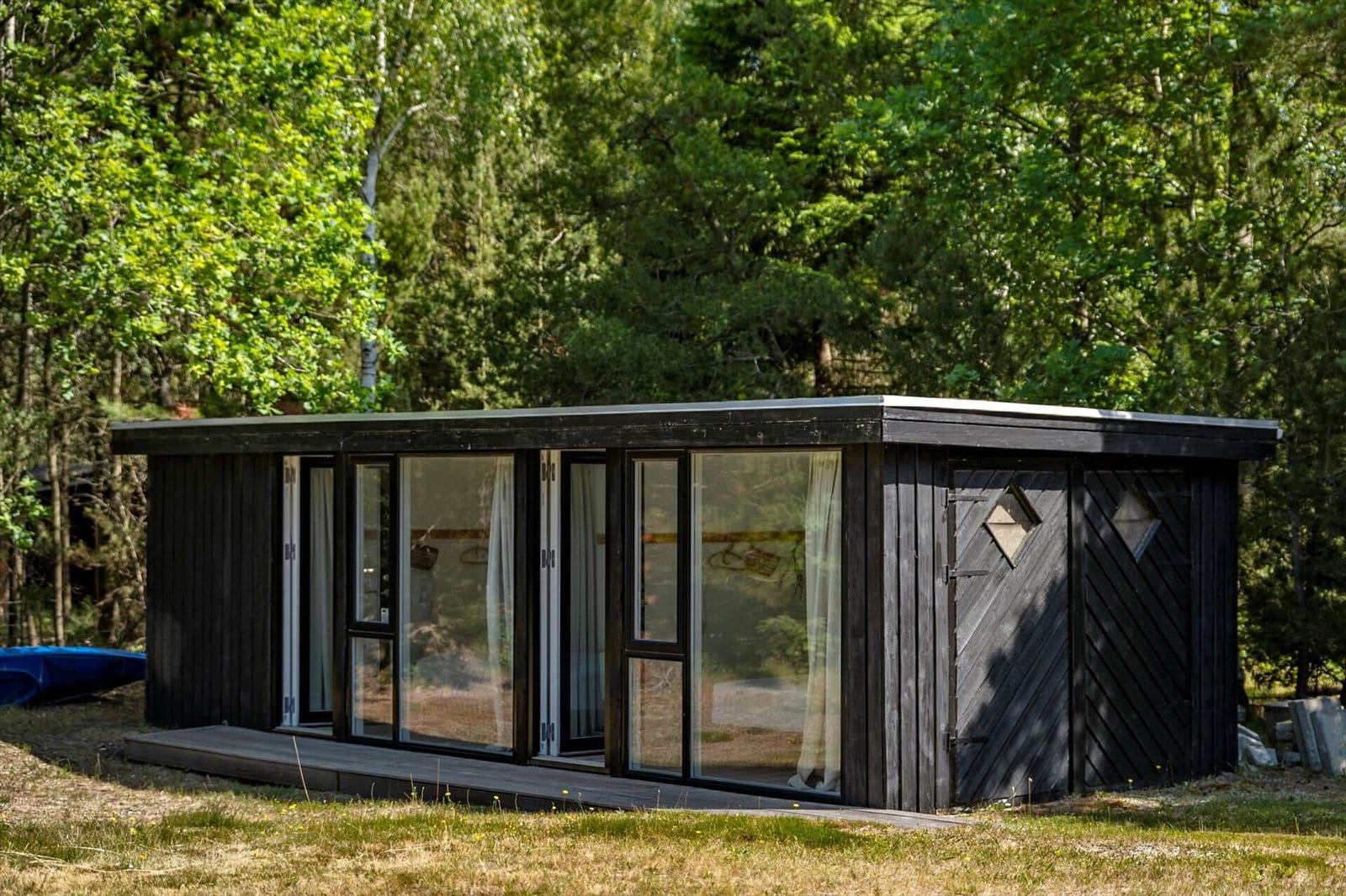 Moderne Holzhütte mit großem Glasfenster und Terrasse im Wald