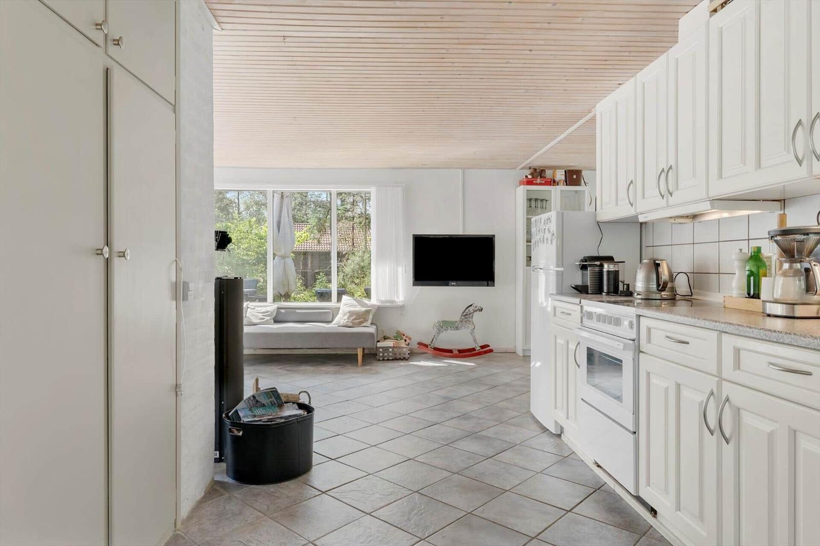 Küche mit weißen Schränken und Blick in Wohnbereich mit Sofa und Fernseher.