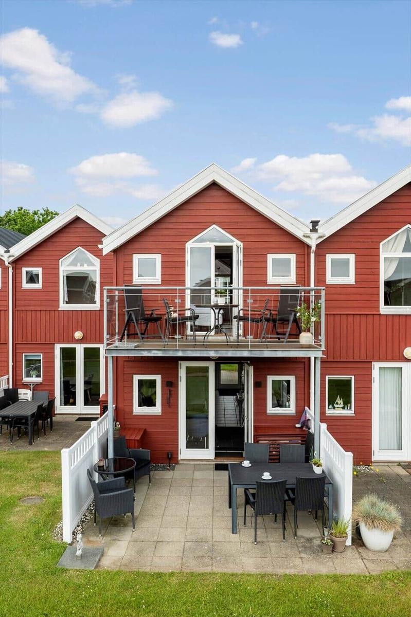 Rotes Haus mit Balkon und Terrasse mit Gartenmöbeln und Pflanzen.