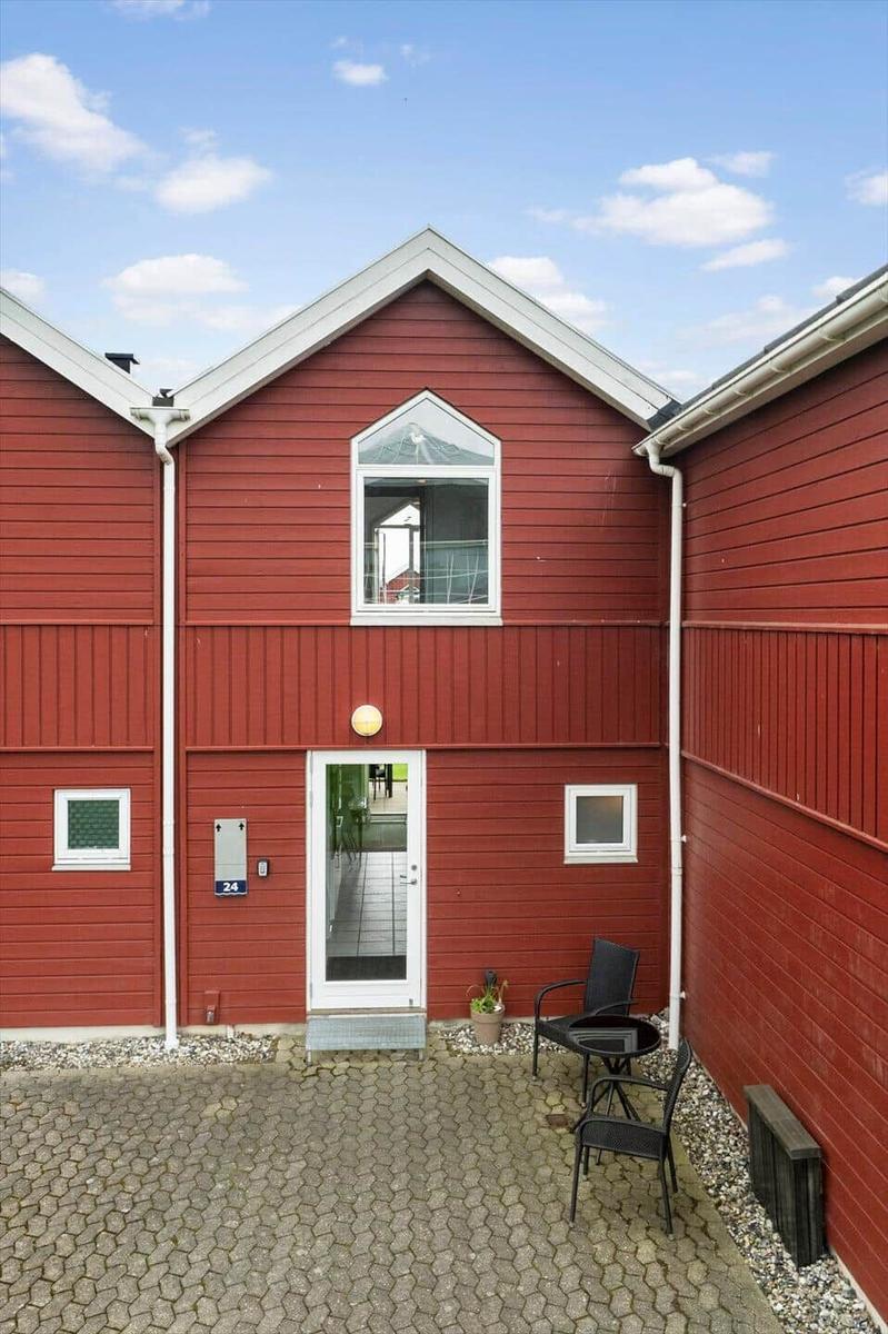 Rotes Holzhaus mit Eingangstür und kleinem Gartenbereich.