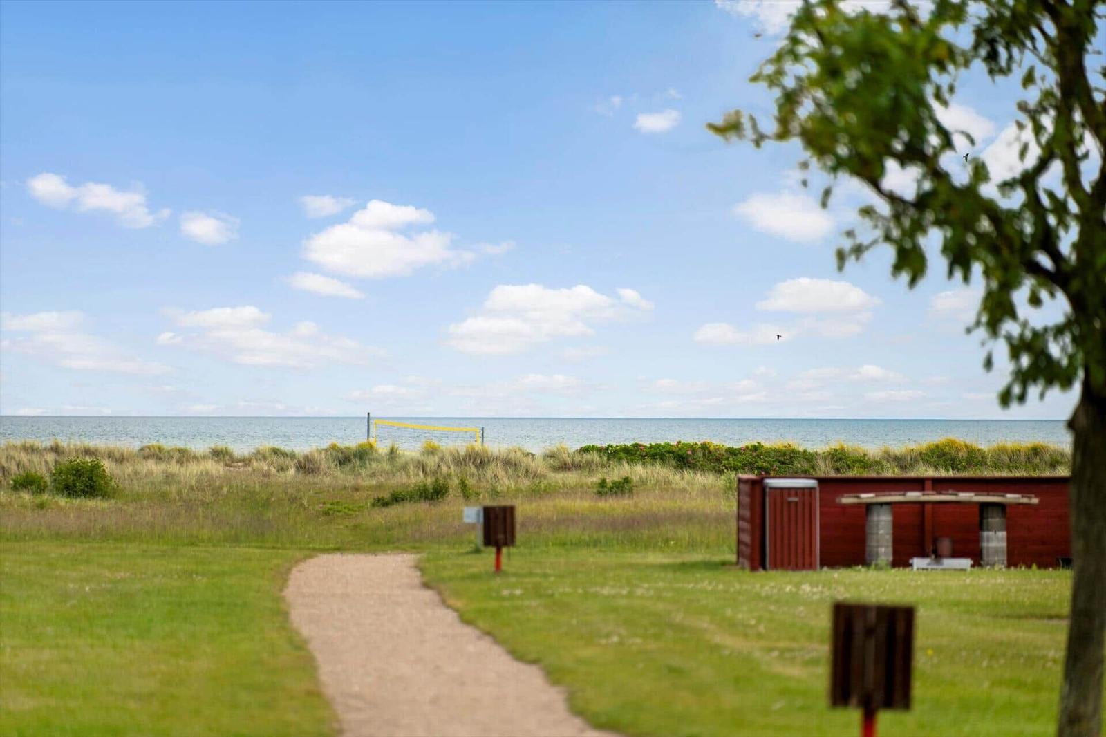 Weg führt zu Strand mit Volleyballnetz und rotem Holzhaus.