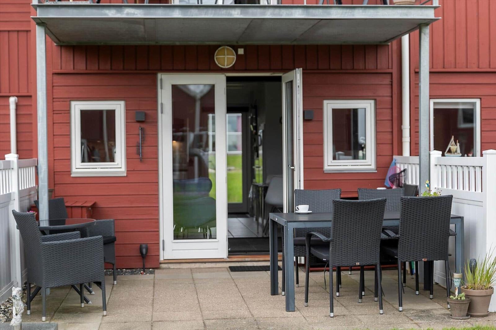 Roter Holzhaus-Eingang mit Terrasse, Tisch, Stühlen und offener Tür.