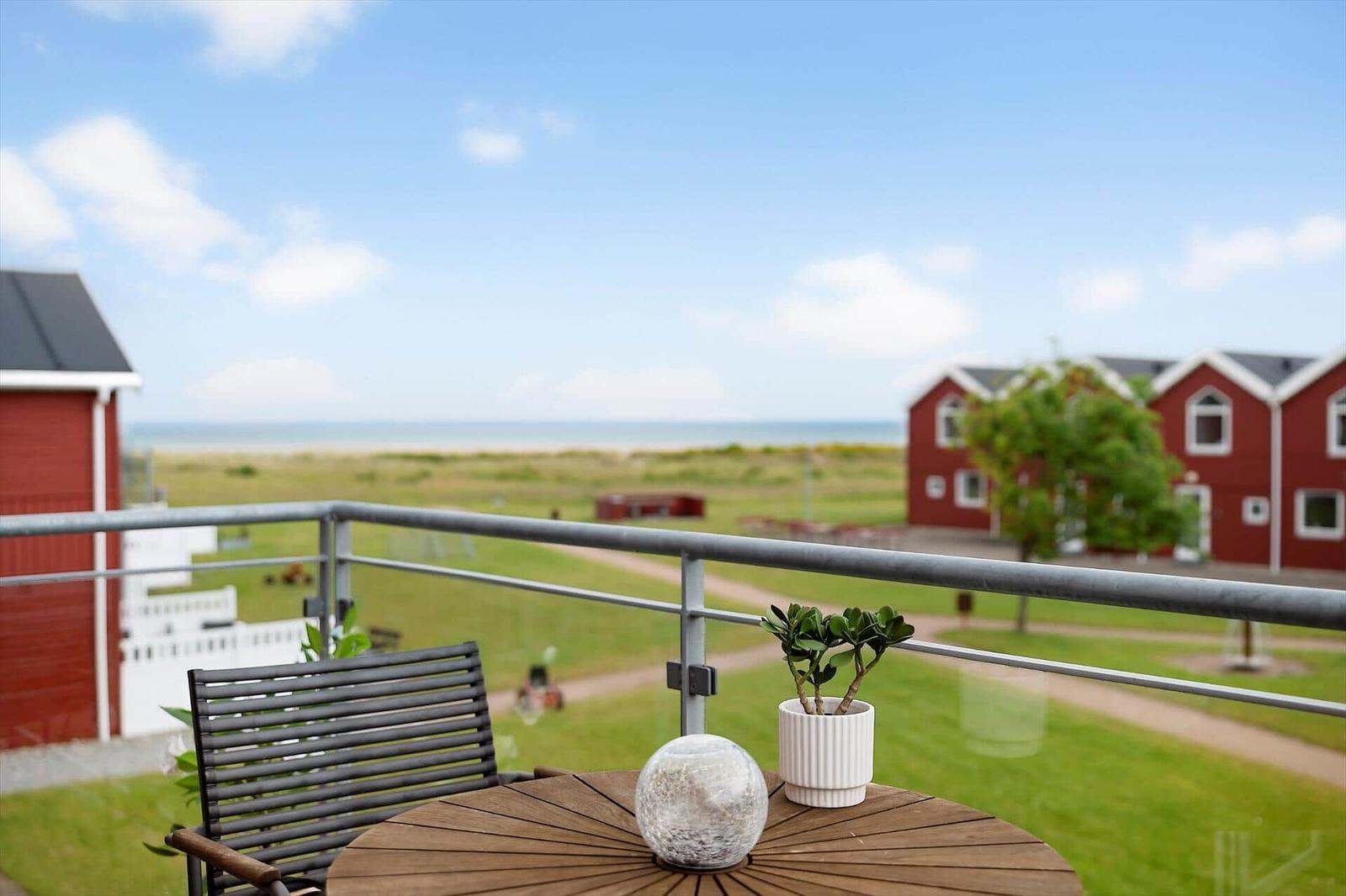 Terrasse mit Tisch und Stuhl, Blick auf Grünfläche und rote Häuser.
