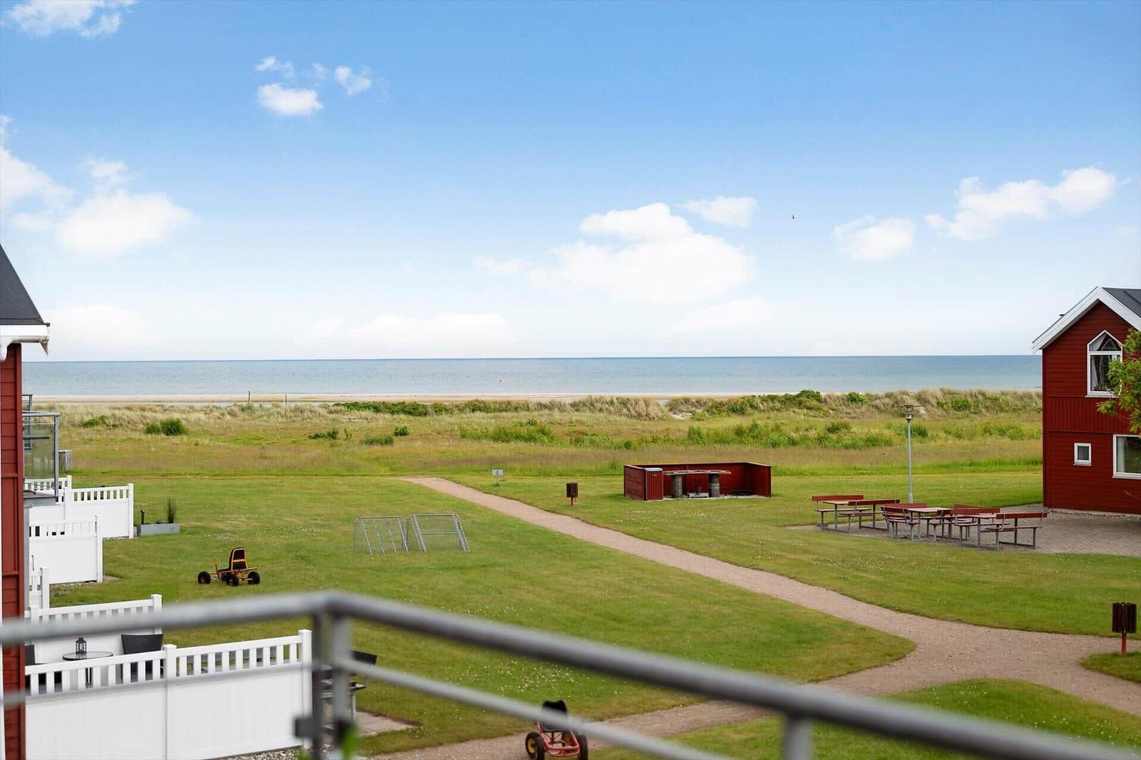 Rote Häuser, grünes Gras und Meer im Hintergrund. Picknicktische und Spielgeräte sind sichtbar.