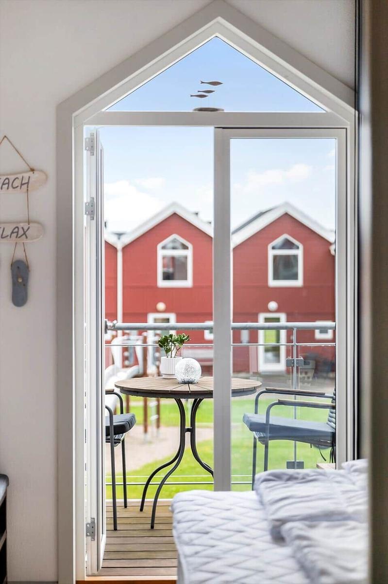 Durch die Glastür blickt man auf eine Terrasse mit Tisch und Stühlen. Im Hintergrund sind rote Häuser zu sehen.