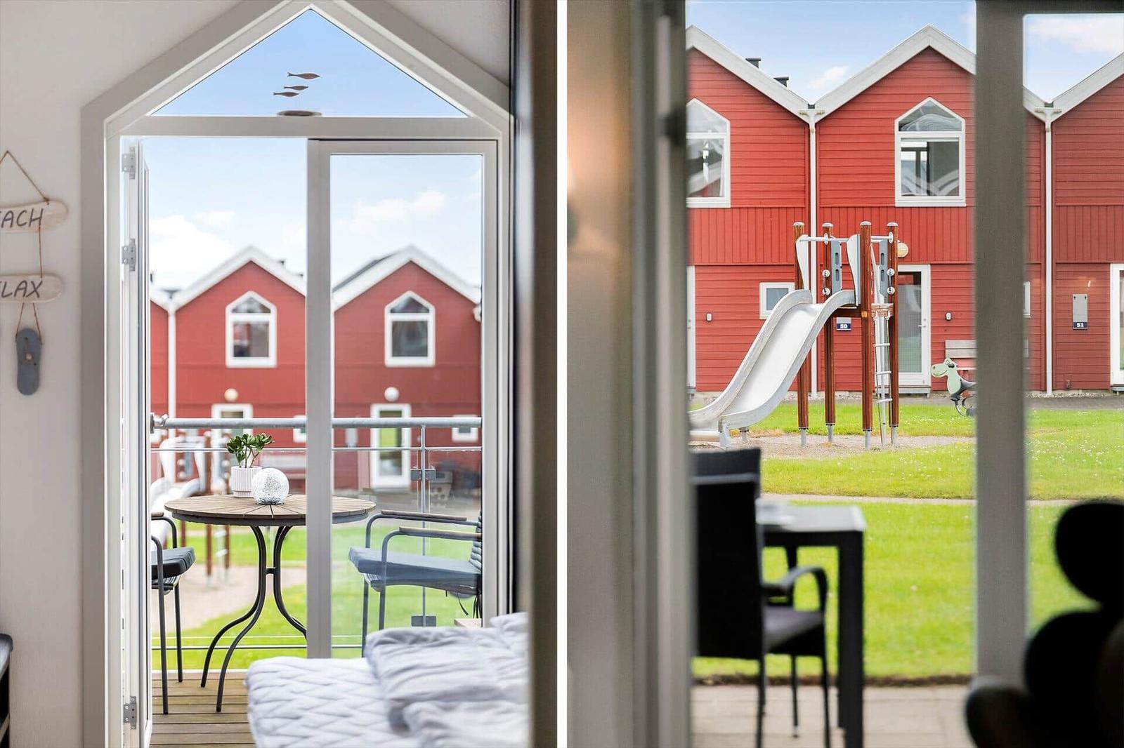 Durch die Glastür ist ein Balkon mit Tisch und Stühlen zu sehen. Im Hintergrund rote Häuser und ein Spielplatz.