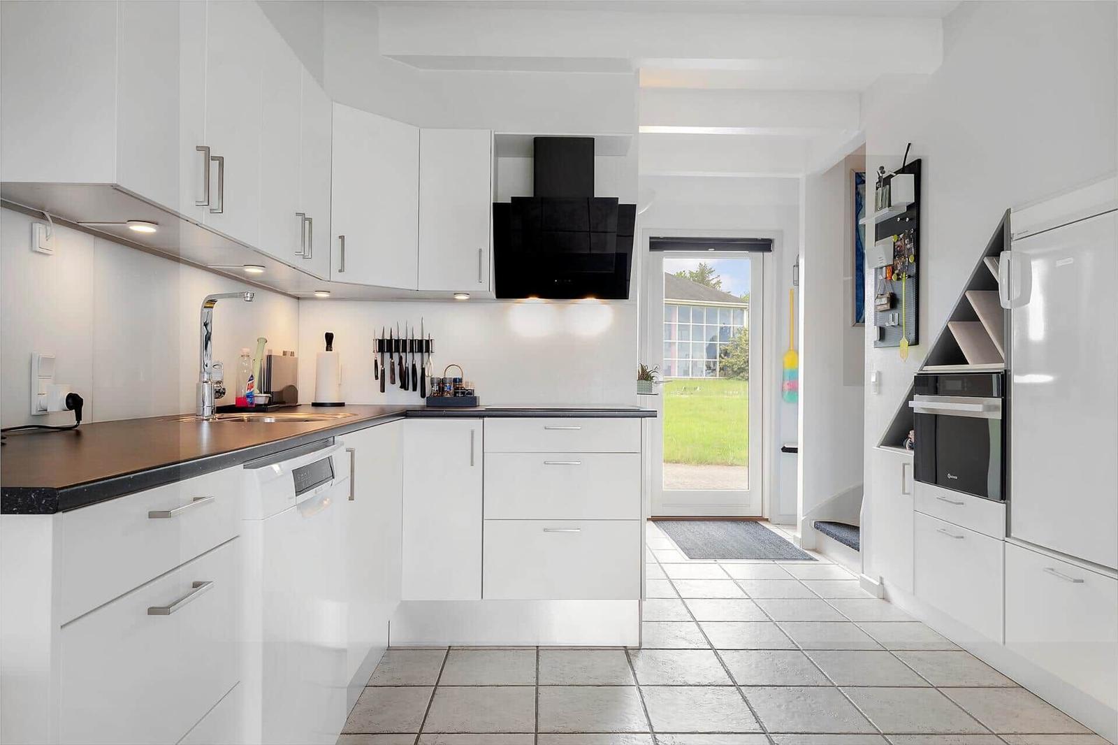 Moderne Küche mit weißen Schränken, schwarzer Arbeitsplatte und Blick auf Garten.