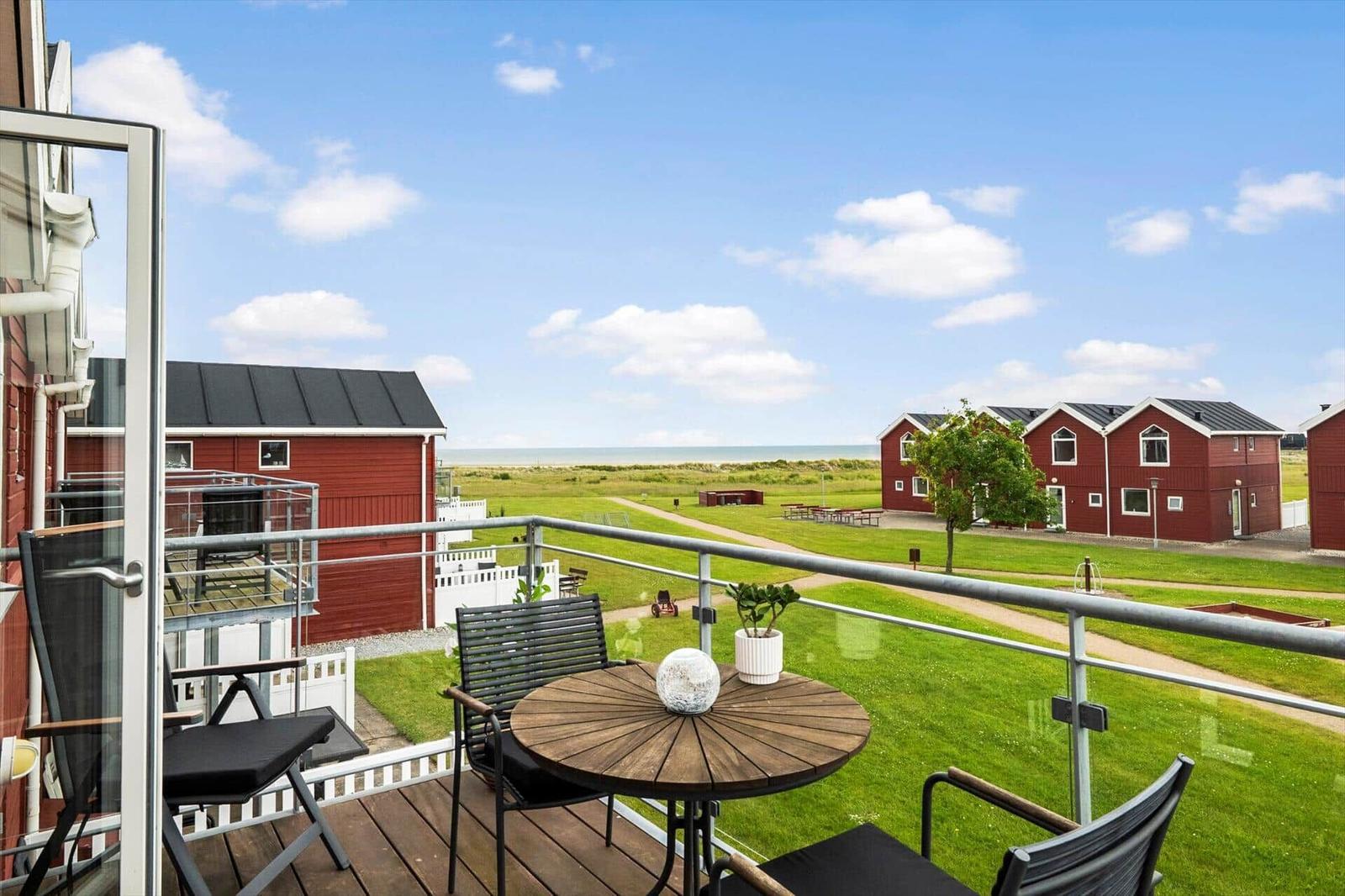 Terrasse mit Tisch und Stühlen. Blick auf grünes Gras und rote Häuser. Horizont über dem Meer.