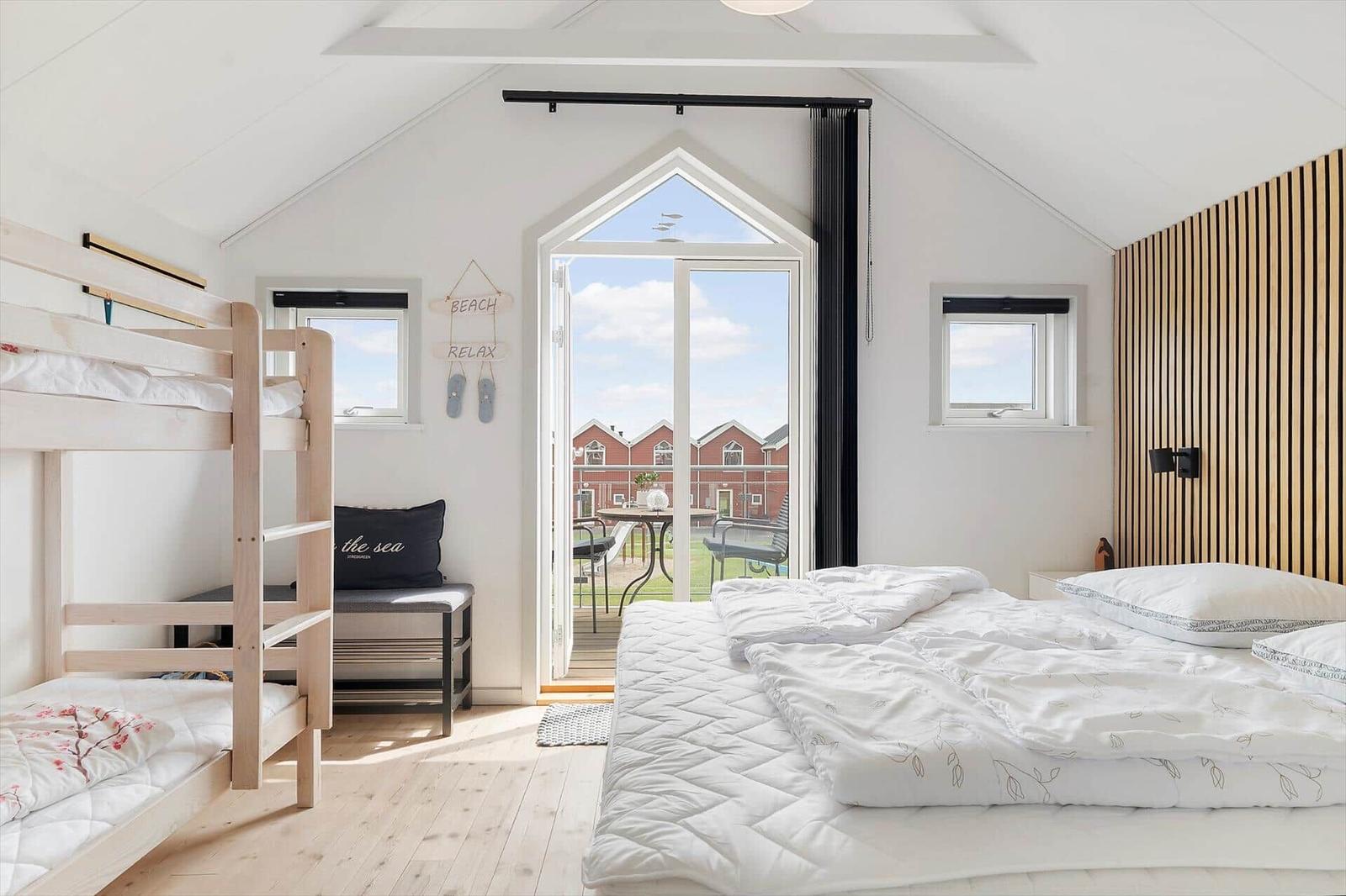 Schlafzimmer mit Doppelbett, Etagenbett und Balkontür. Holzwand und hölzerner Boden.